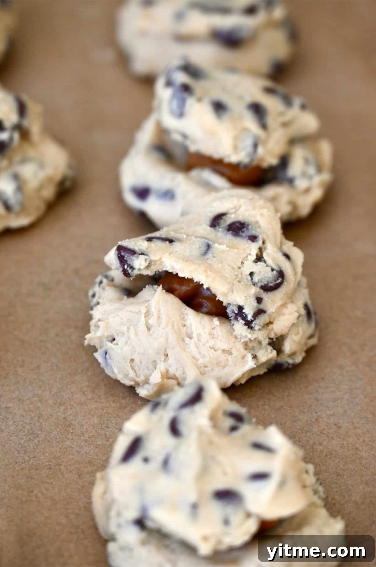 Caramel Lava Chocolate Chip Cookies 7 Cookie dough balls stuffed with soft caramels on a baking sheet lined with parchment paper.