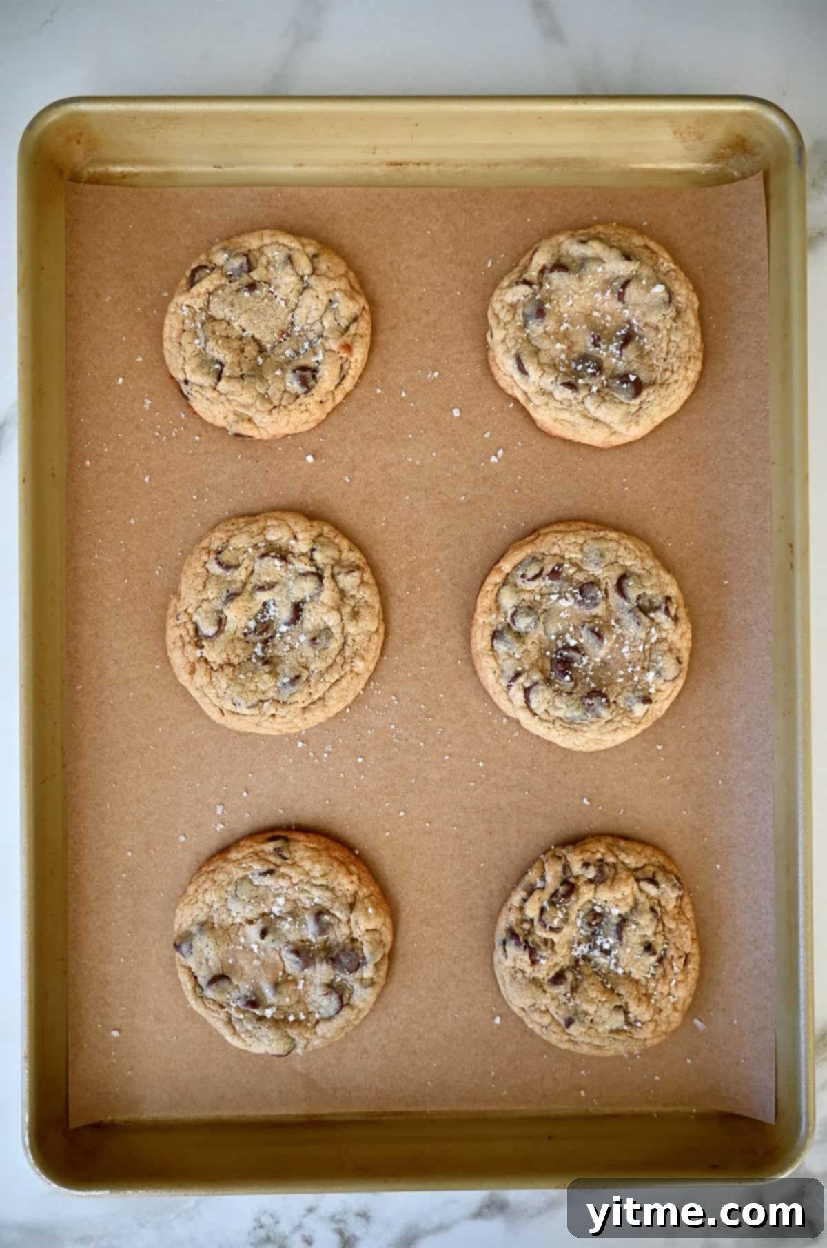 Caramel Lava Chocolate Chip Cookies 8 Freshly baked caramel cookies on a parchment paper-lined baking sheet.