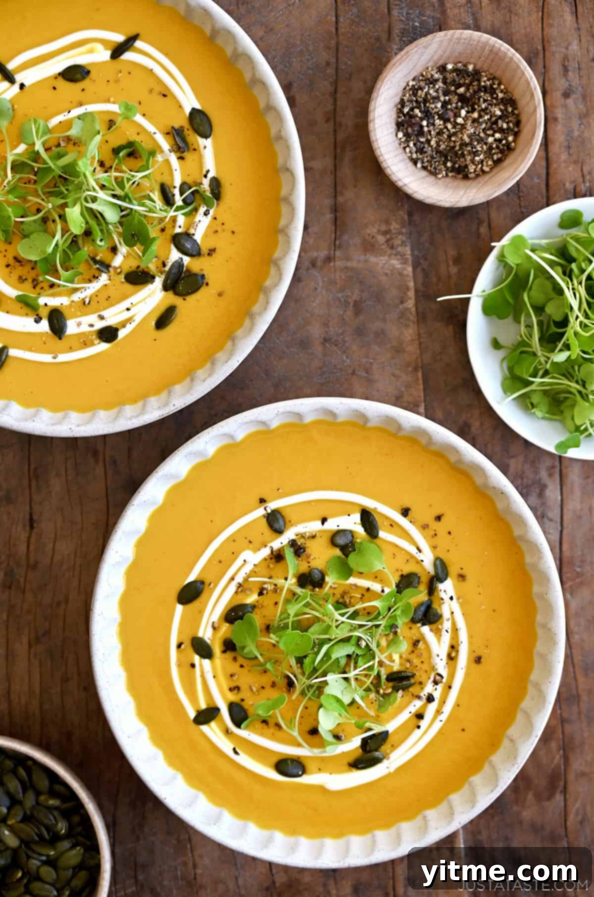 Two bowls of Thai coconut pumpkin soup garnished with pumpkin seeds and micro greens.