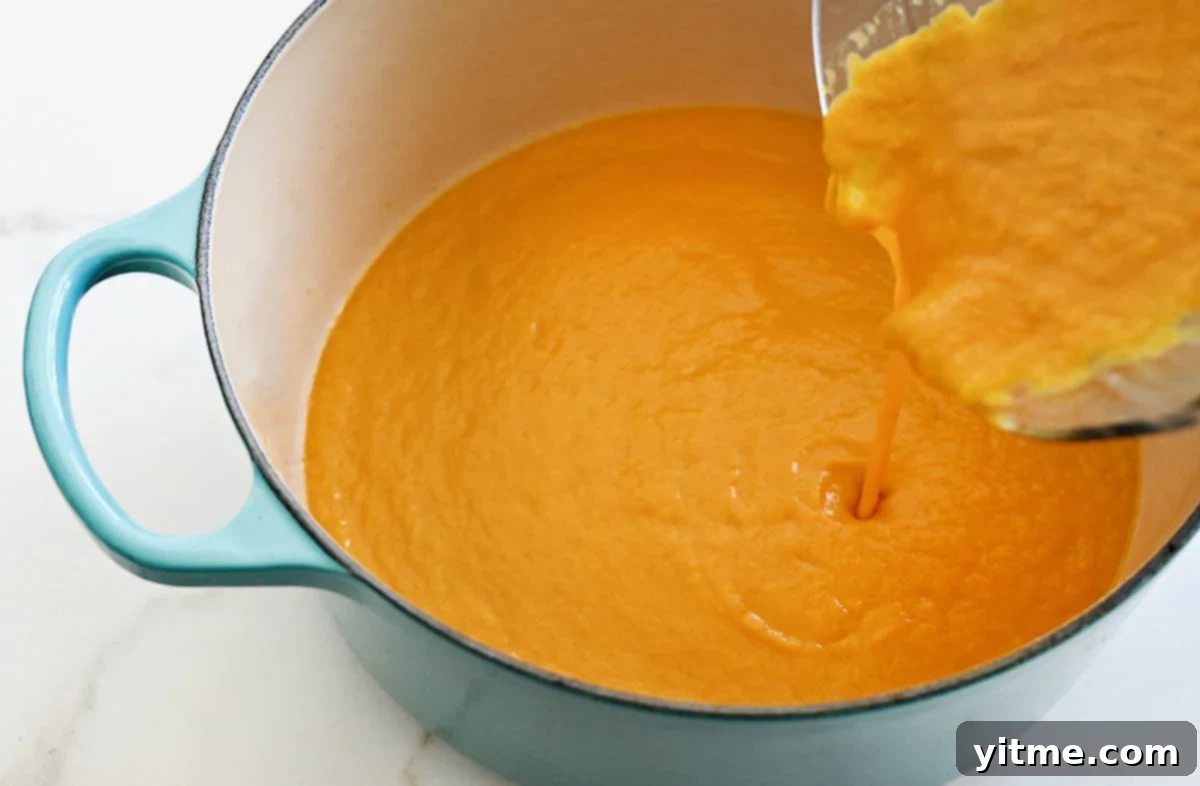 Pumpkin soup being poured from a blender into a large stockpot.