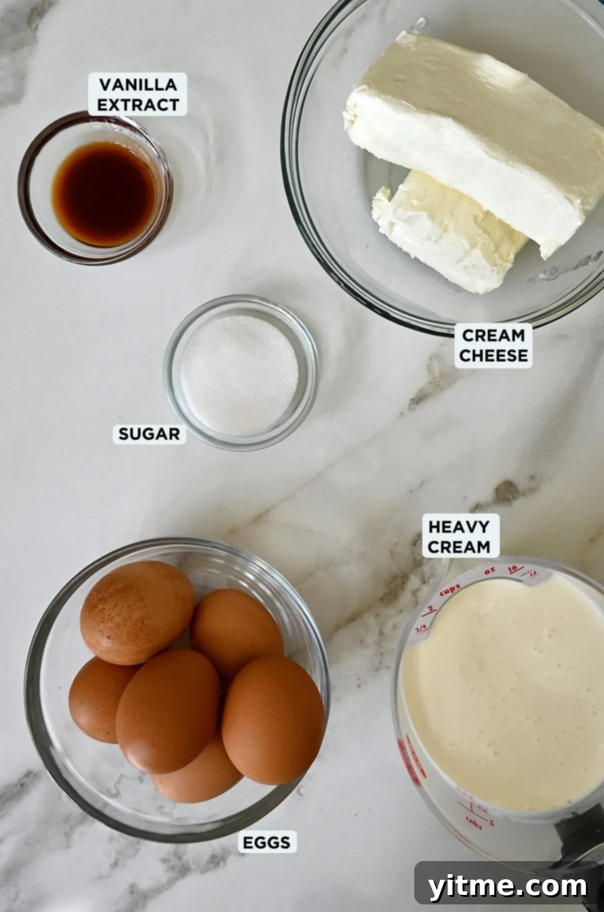 Five bowls containing vanilla extract, cream cheese, sugar, heavy cream and eggs.