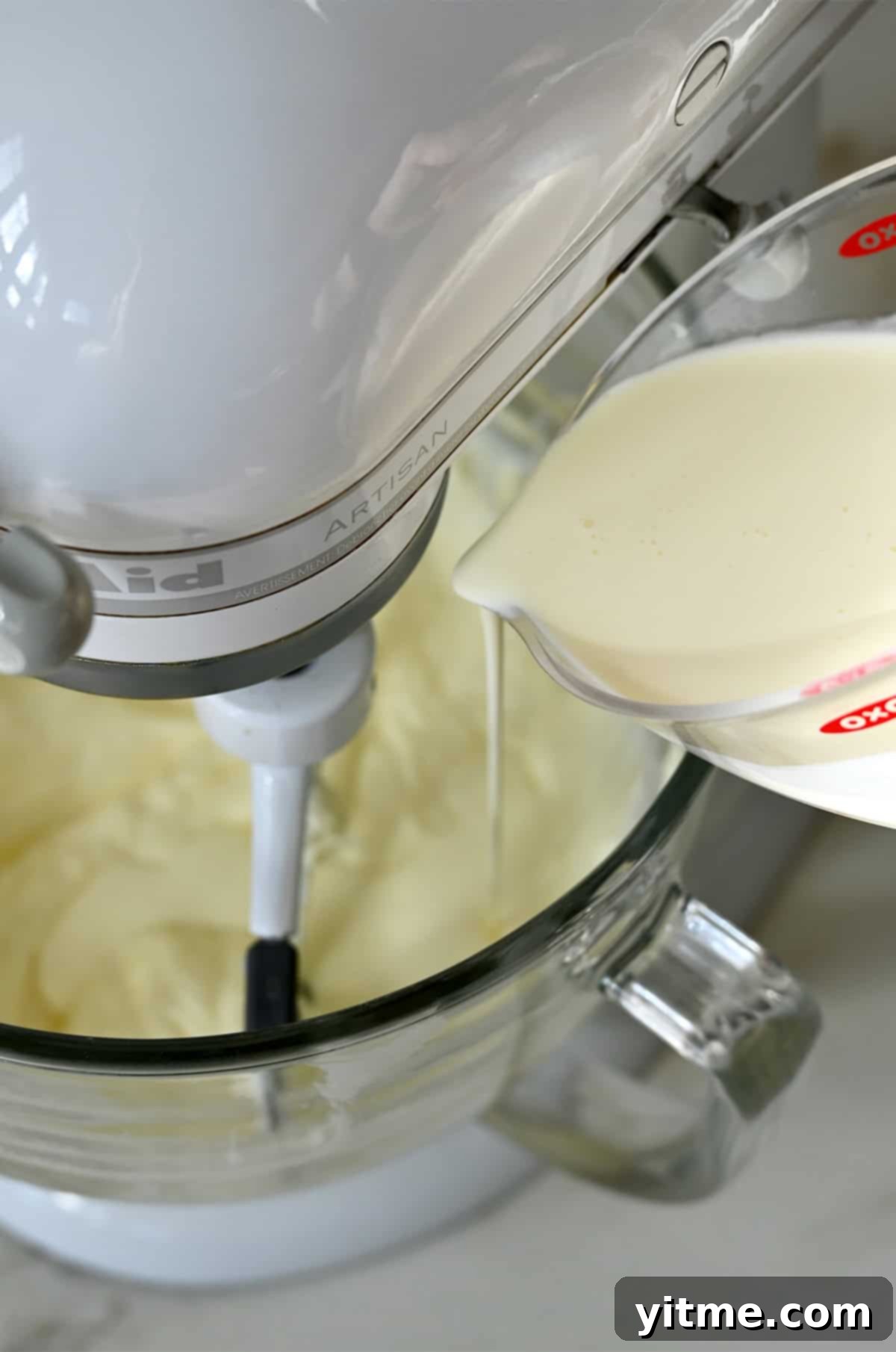 Streaming heavy cream into the bowl of a stand mixer with cream cheese and sugar.