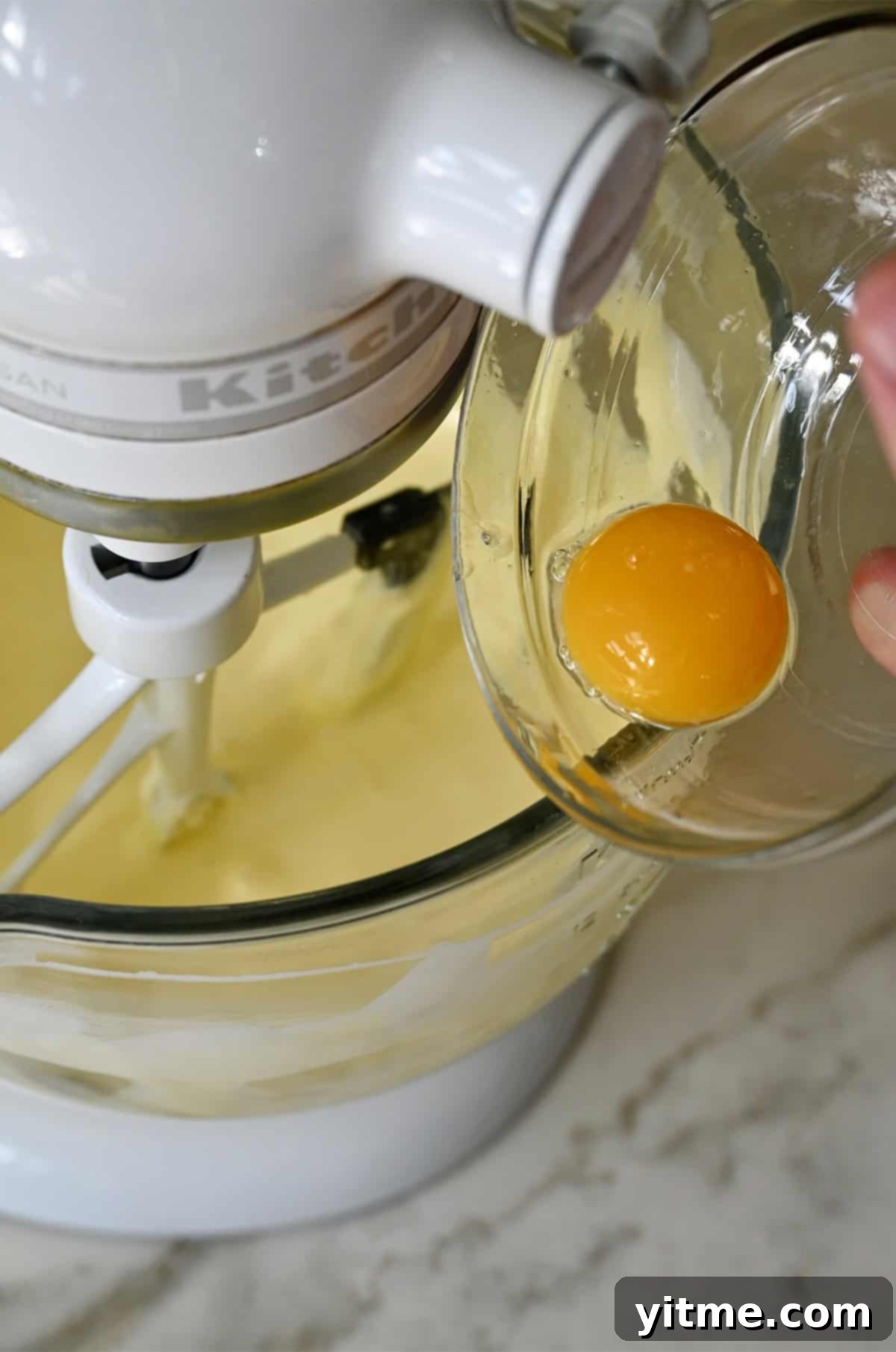 Adding one egg yolk to the bowl of a stand mixer with cream cheese, sugar and heavy cream to make a custard.