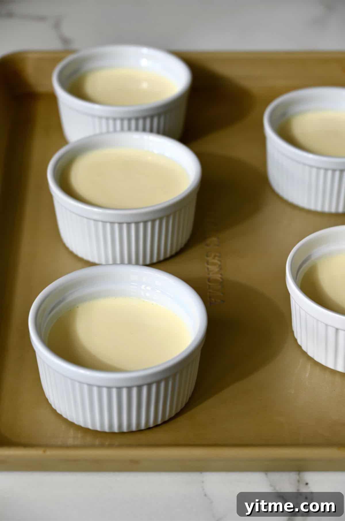 Ramekins filled with custard in a water bath.