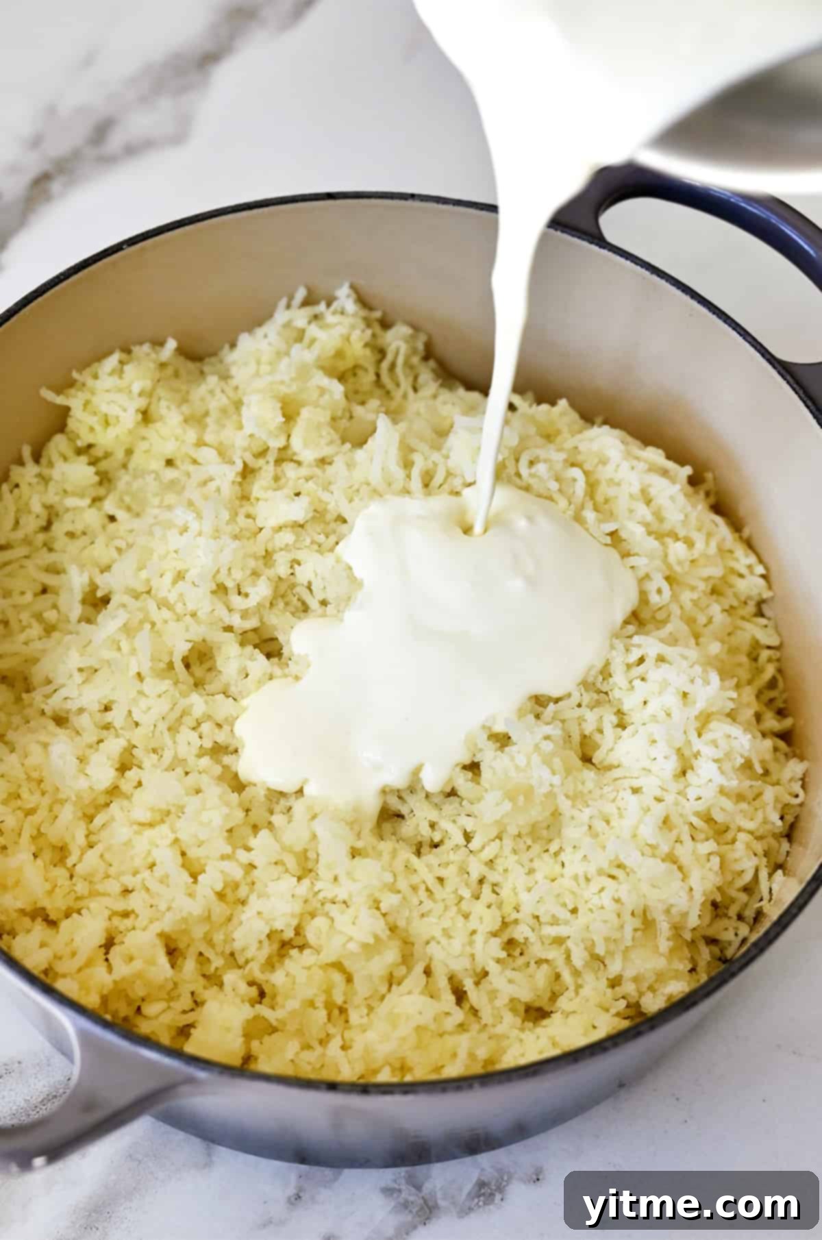 Ultimate Creamy Dream: The Mashed Potato Revelation 5 Riced potatoes in a large stockpot with heavy cream being poured into the pot.