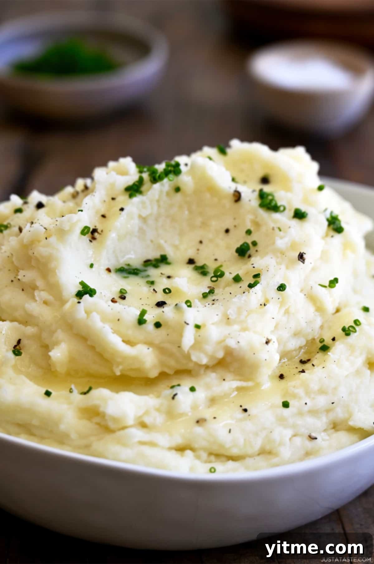 Ultimate Creamy Dream: The Mashed Potato Revelation 6 Creamy mashed potatoes topped with chives, black pepper and butter in a large serving bowl.
