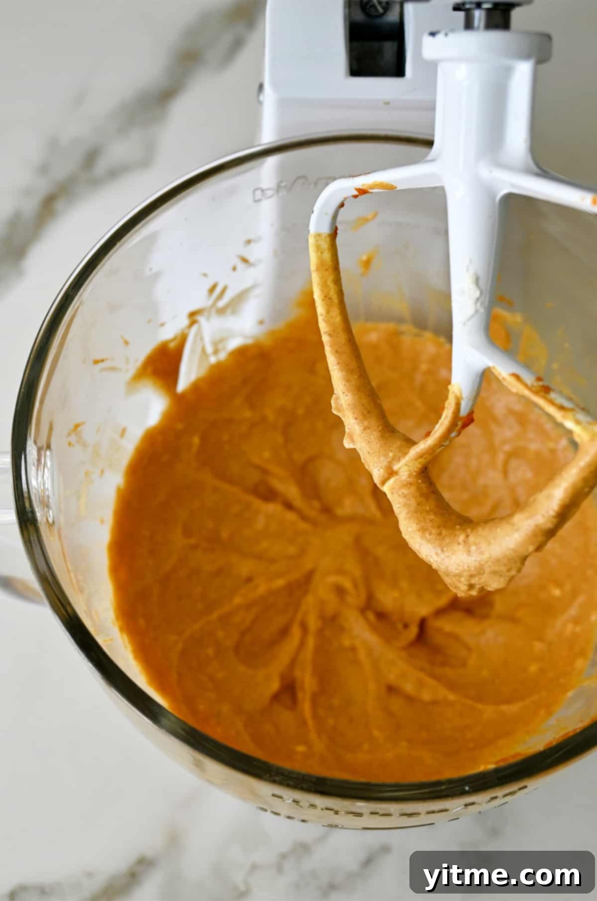 A stand mixer with pumpkin cheesecake filling in the bowl.