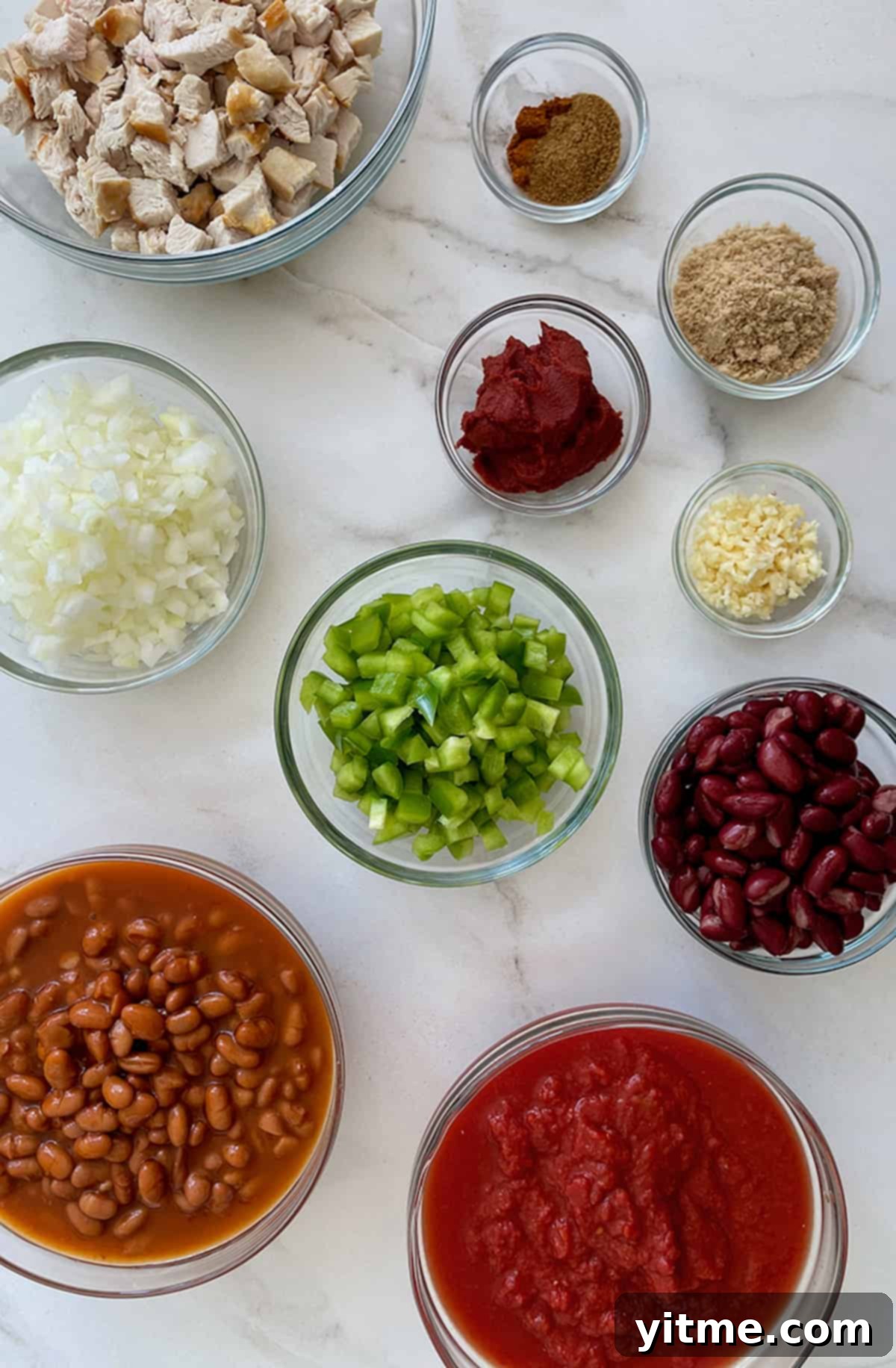 Various sizes of clear bowls containing perfectly chopped turkey, rich tomato paste, aromatic minced garlic, a selection of savory seasonings, sweet brown sugar, fresh diced green pepper, hearty kidney beans, creamy pinto beans, crushed tomatoes for the base, and finely diced onions, all laid out for the 30-minute turkey chili recipe.