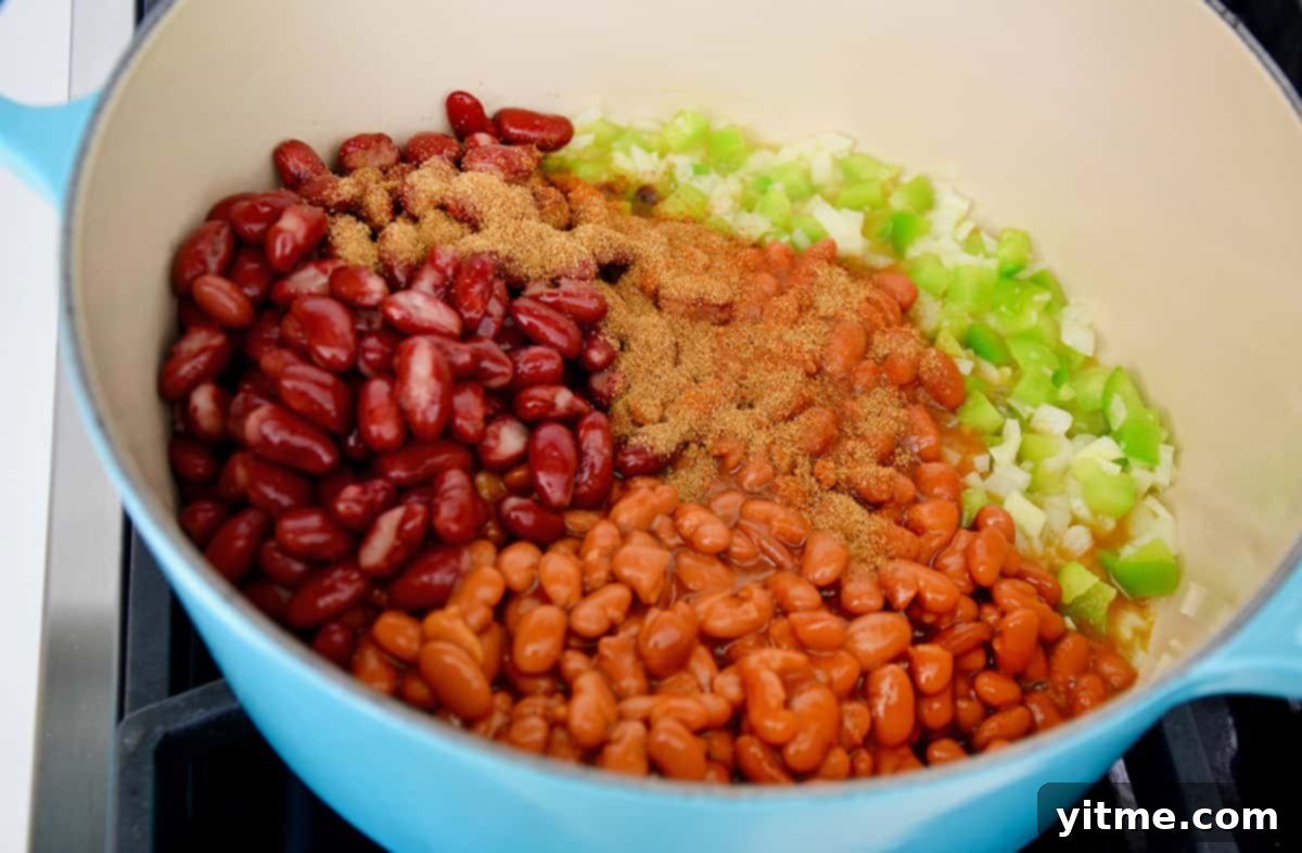 A vibrant blue Dutch oven containing perfectly sautéed onions and peppers, ready for the next step, topped with hearty kidney beans, flavorful pinto beans, and a sprinkle of seasonings for the delicious turkey chili.