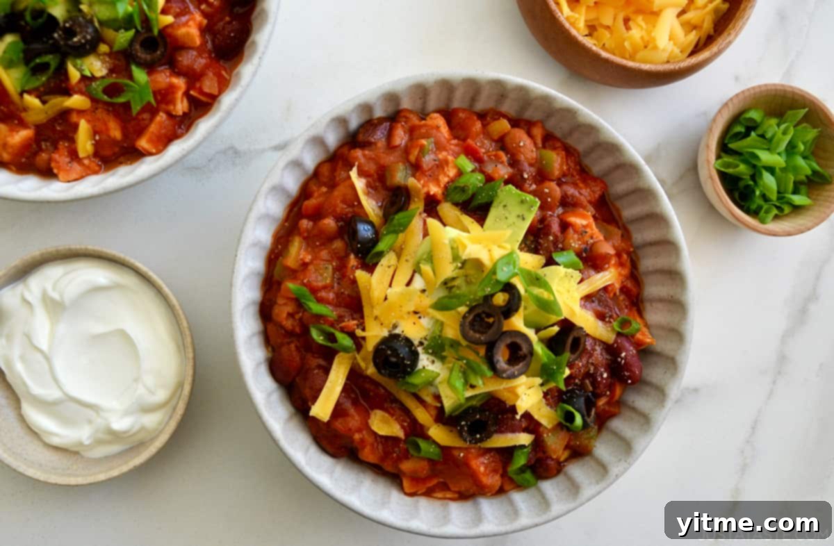 A beautifully presented bowl of hearty turkey chili, generously topped with cool, creamy sour cream, a sprinkle of savory shredded cheese, a handful of briny black olives, and fresh diced avocado for a perfect finish.