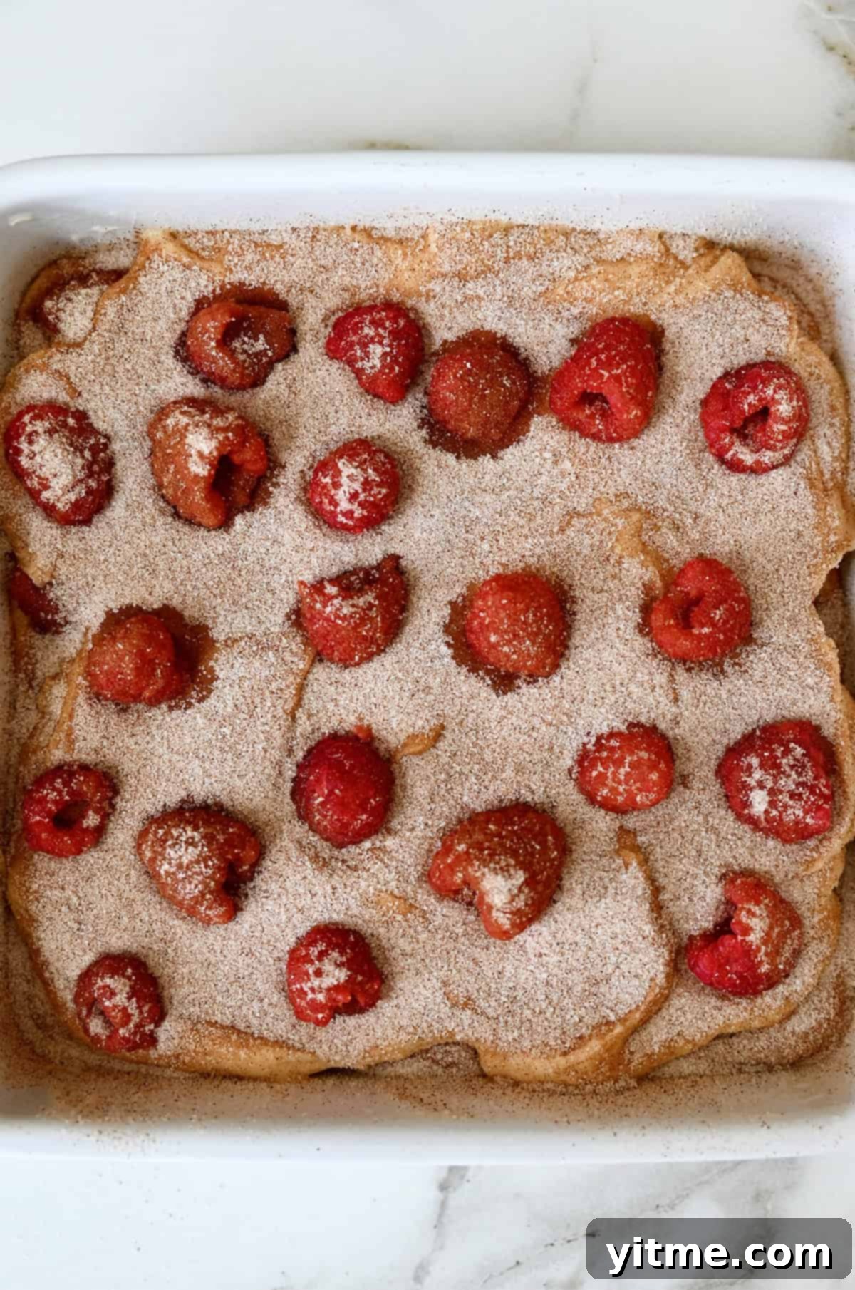 The second layer of coffee cake batter in a 9-inch square baking pan topped with cinnamon sugar and fresh raspberries.