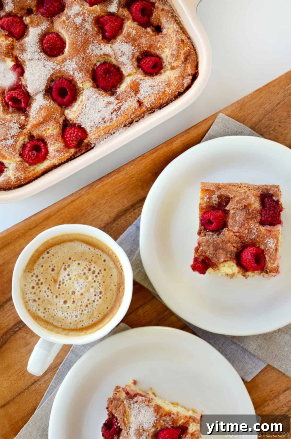 A latte next to two slices of sour cream coffee cake with raspberries on white plates.