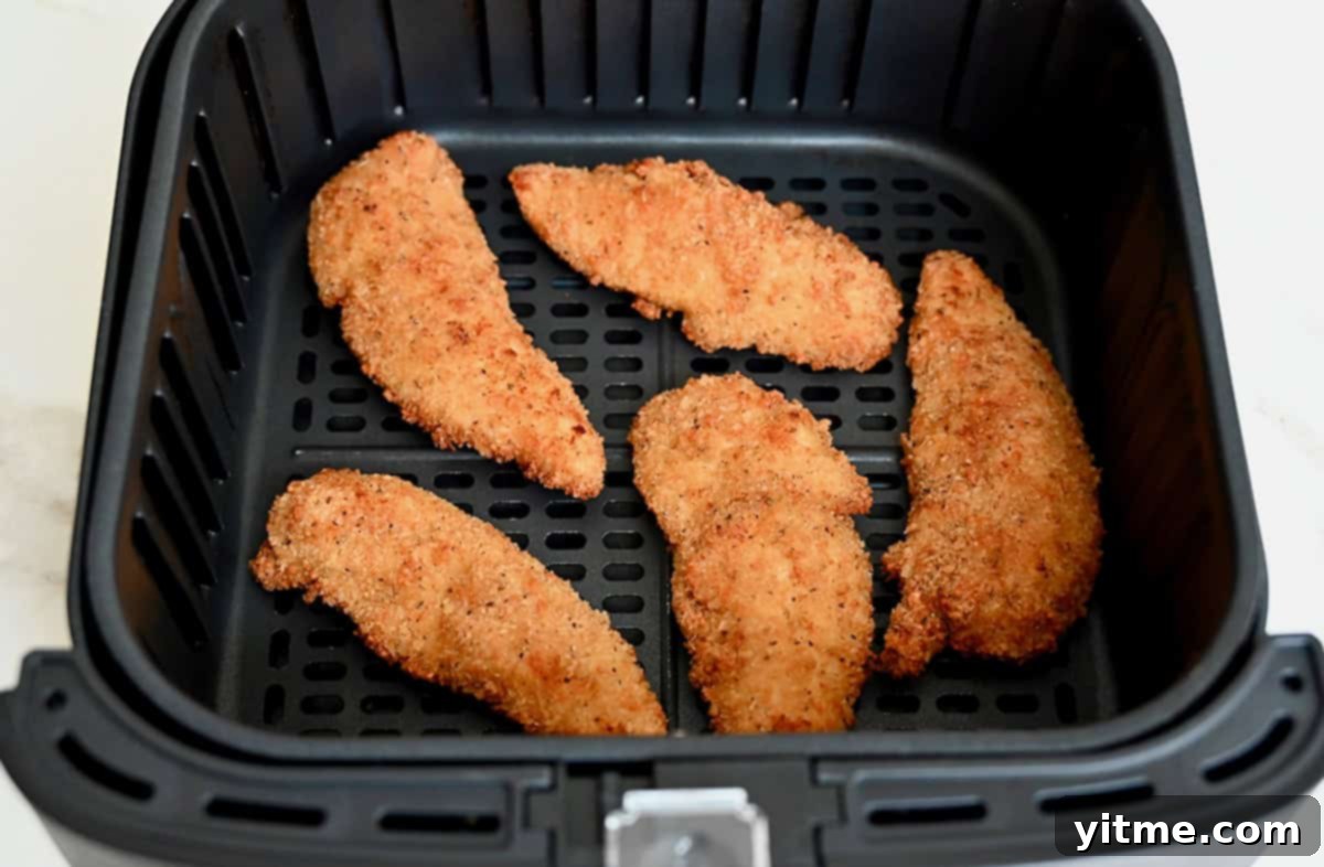 Crispy chicken tenders in the basket of an air fryer.