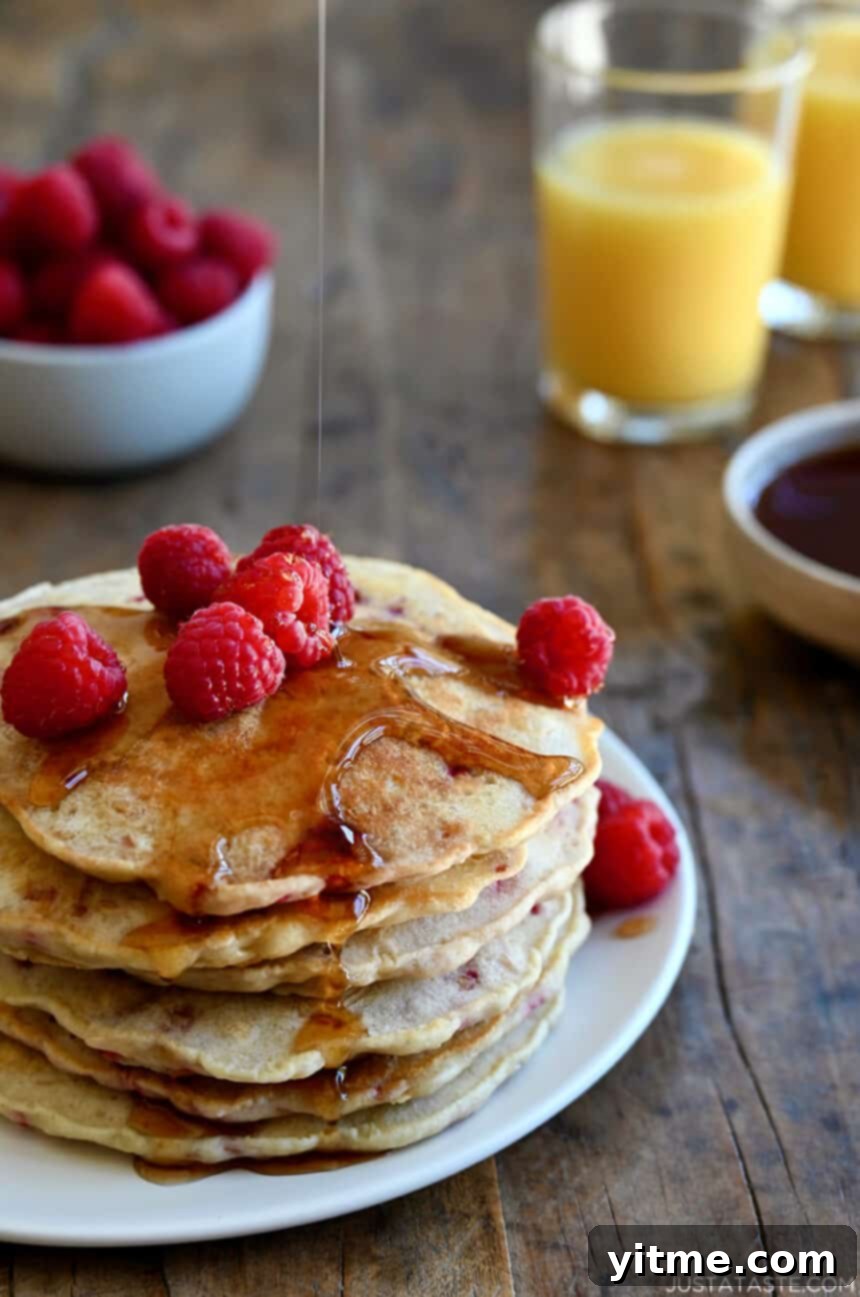 A tall stack of Raspberry Oatmeal Pancakes topped with maple syrup and fresh raspberries