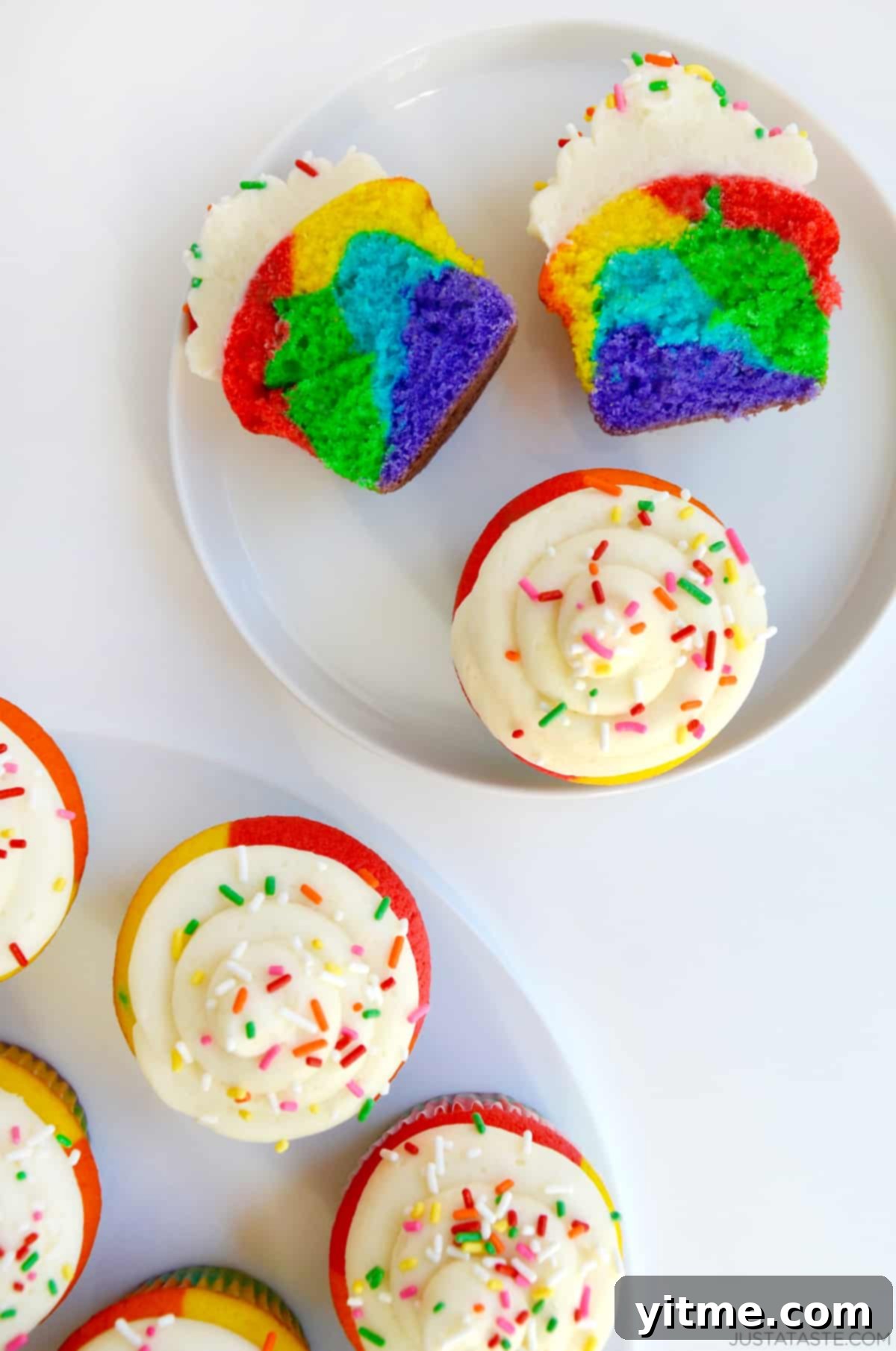 Rainbow cupcake cut in half revealing vibrant layers, with more cupcakes in the background