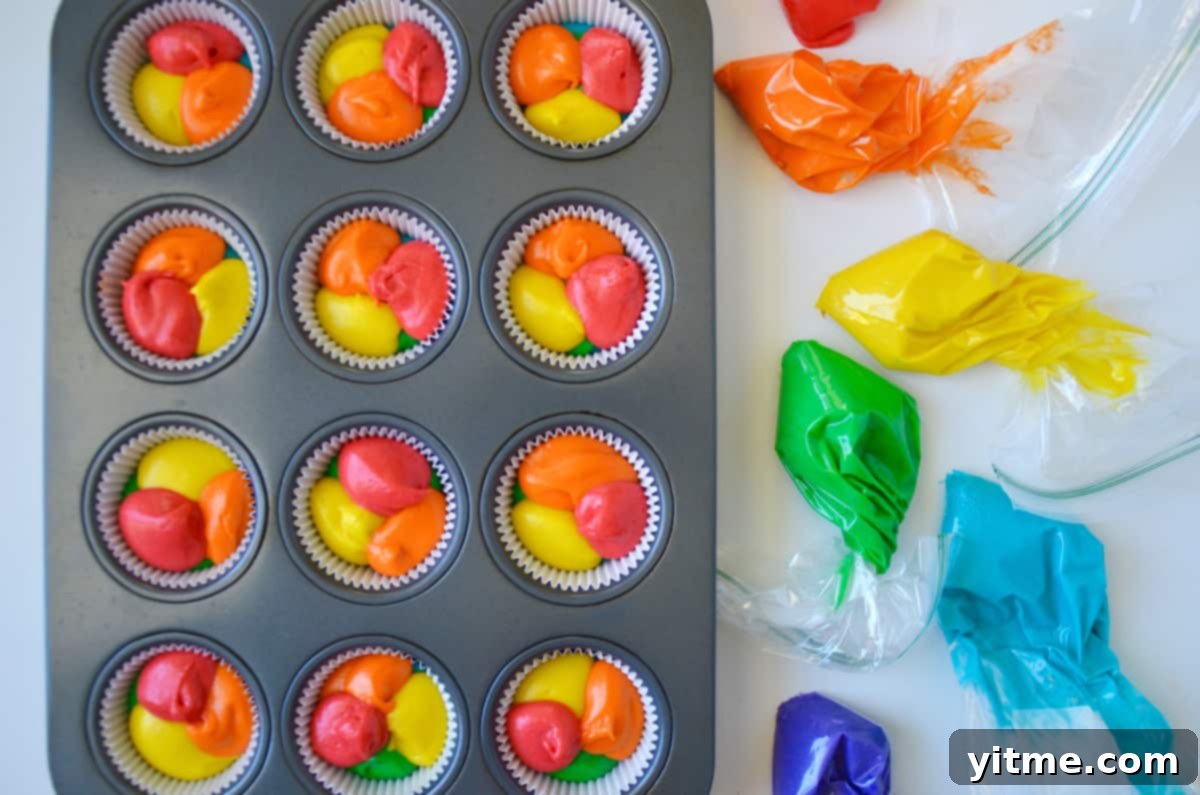 Cupcake wrappers filled with rainbow colored batter, and piping bags with batter