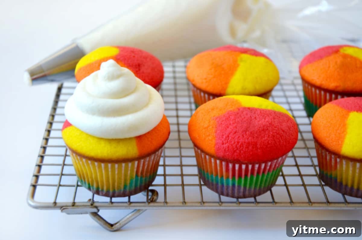 Rainbow cupcakes cooling, one being frosted with buttercream
