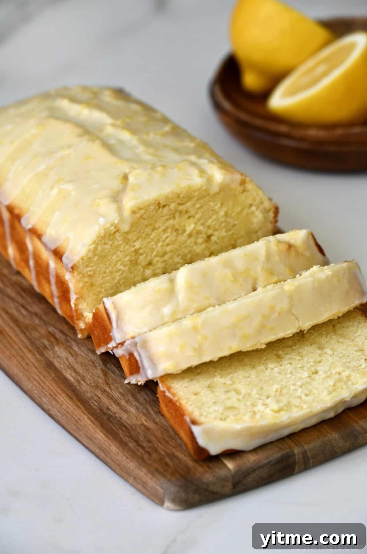 Slices of a perfectly moist glazed lemon loaf on a rustic small wood cutting board, ready to be served.
