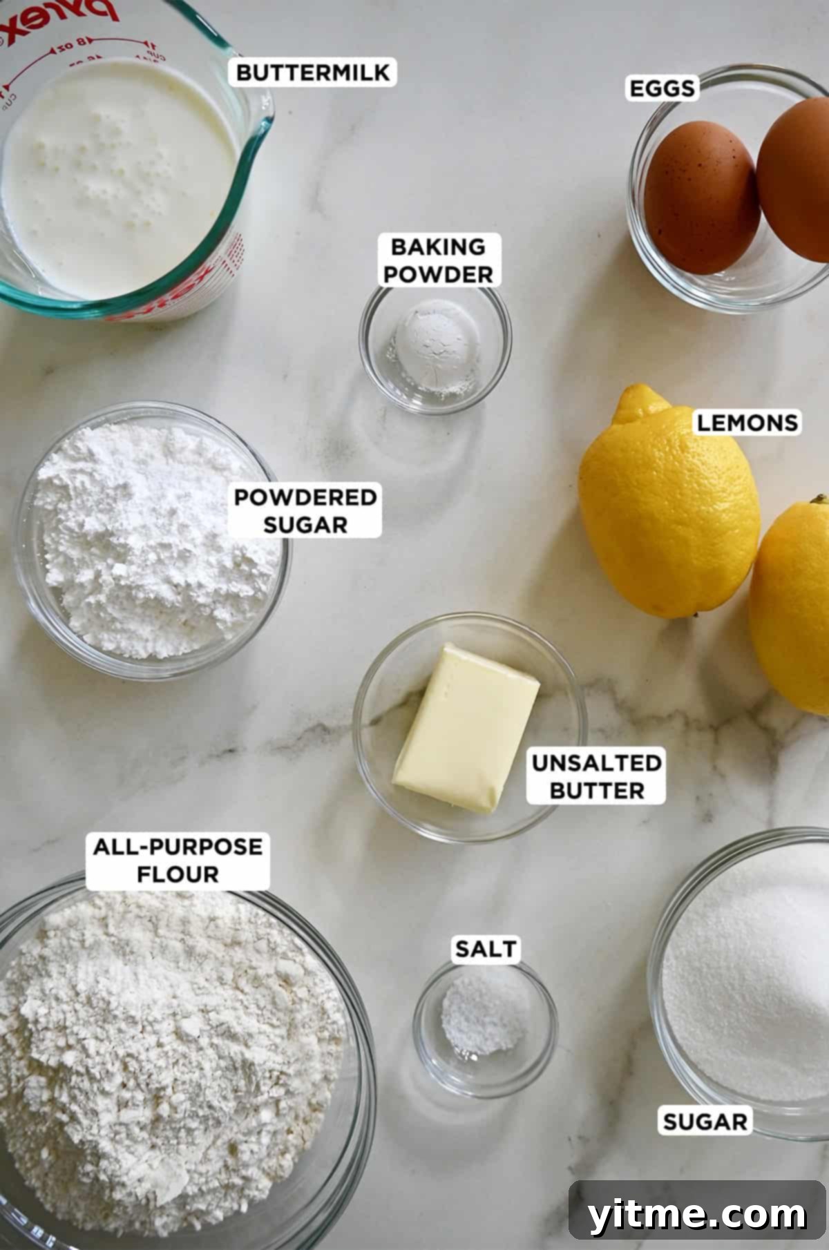 Fresh lemons next to bowls of flour, sugar, and butter, prepared for baking lemon bread.