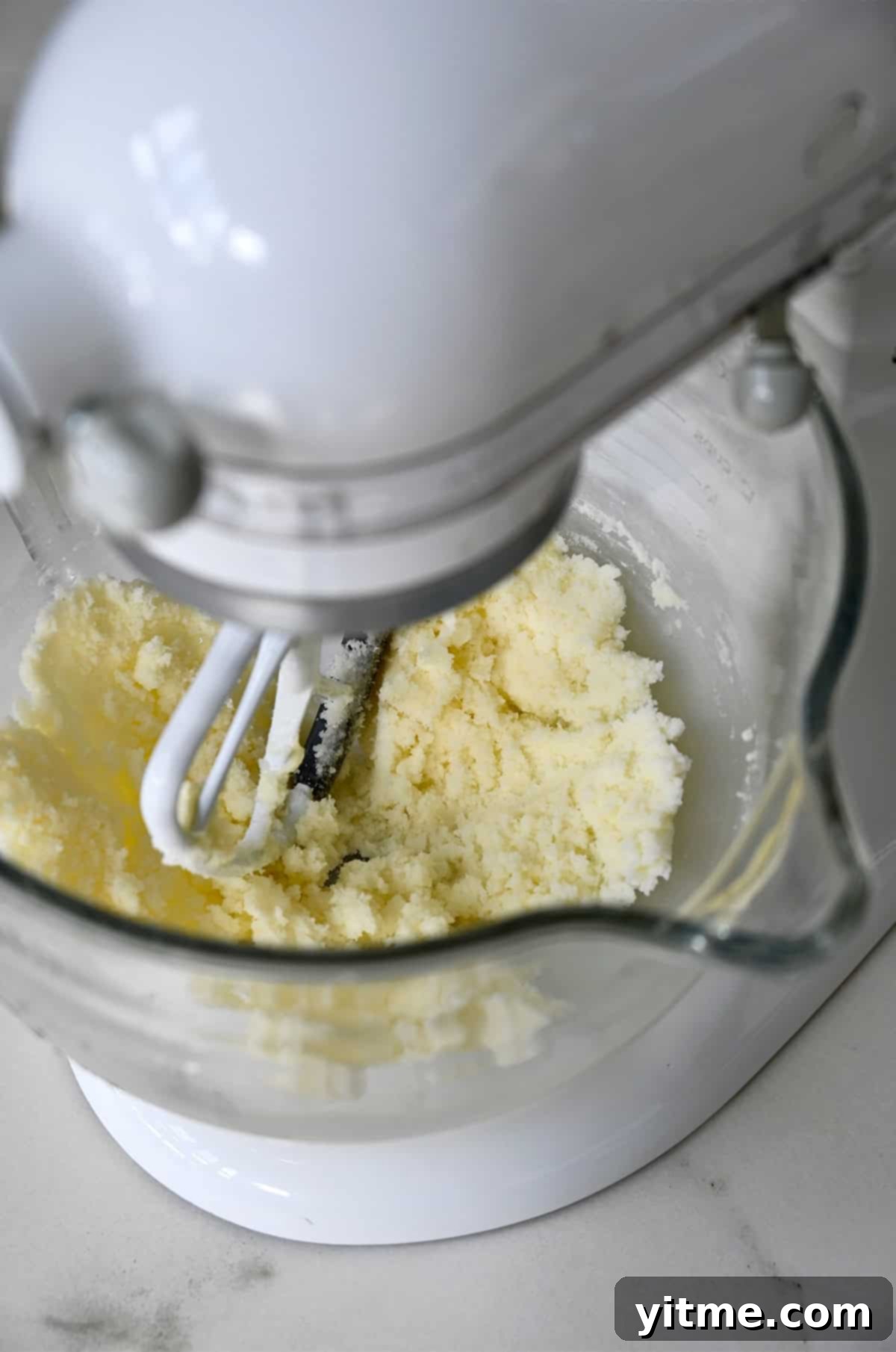 A stand mixer creaming together softened butter and granulated sugar with a paddle attachment.