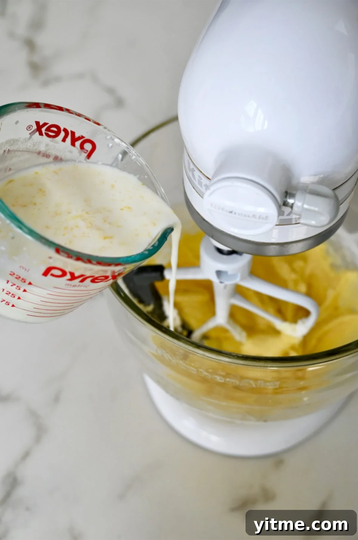 Pouring the buttermilk, lemon juice, and lemon zest mixture from a measuring cup into the stand mixer with the creamed butter and sugar.
