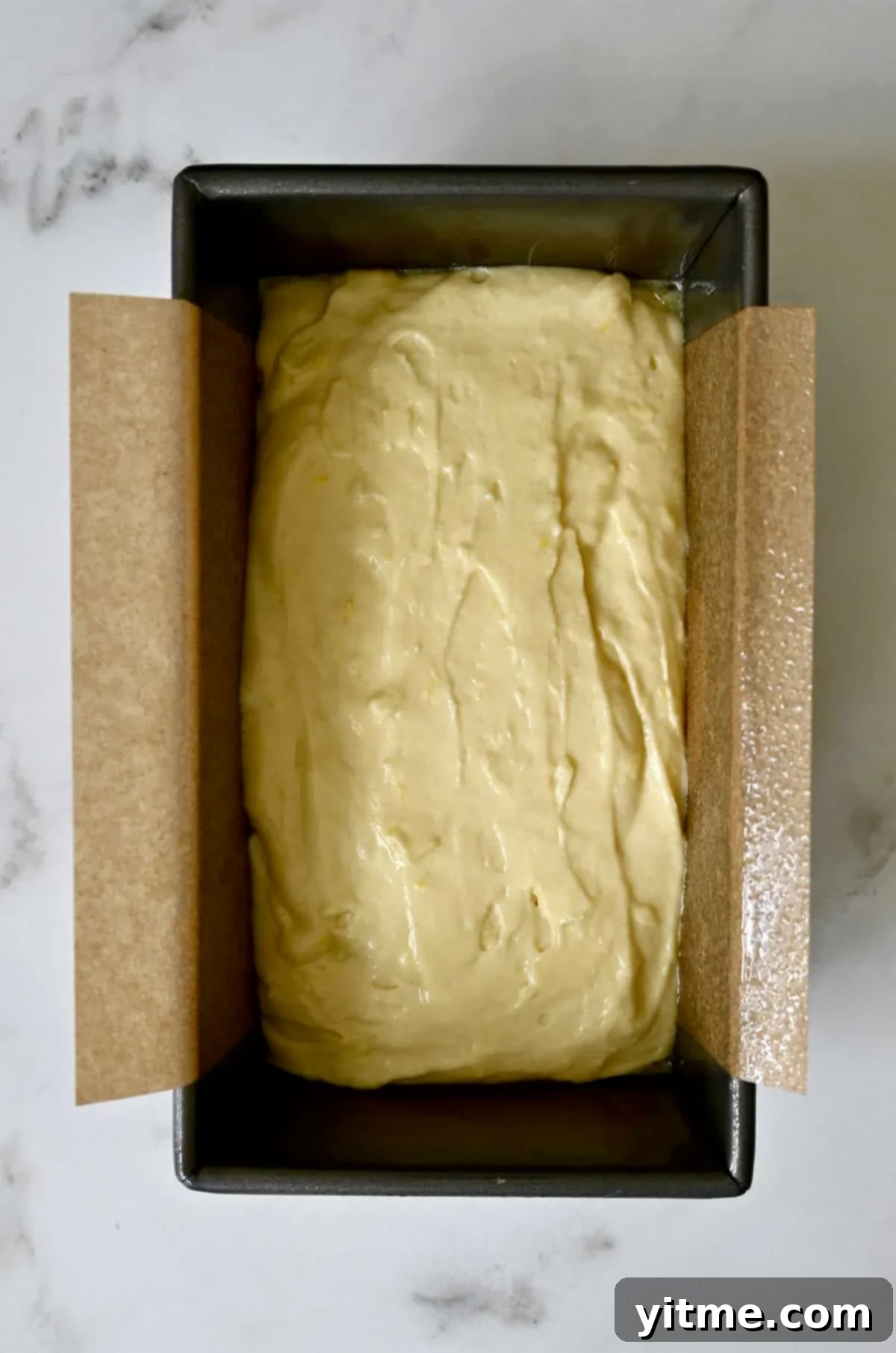 Unbaked lemon bread batter evenly spread in a 9x5 inch loaf pan, lined with parchment paper.