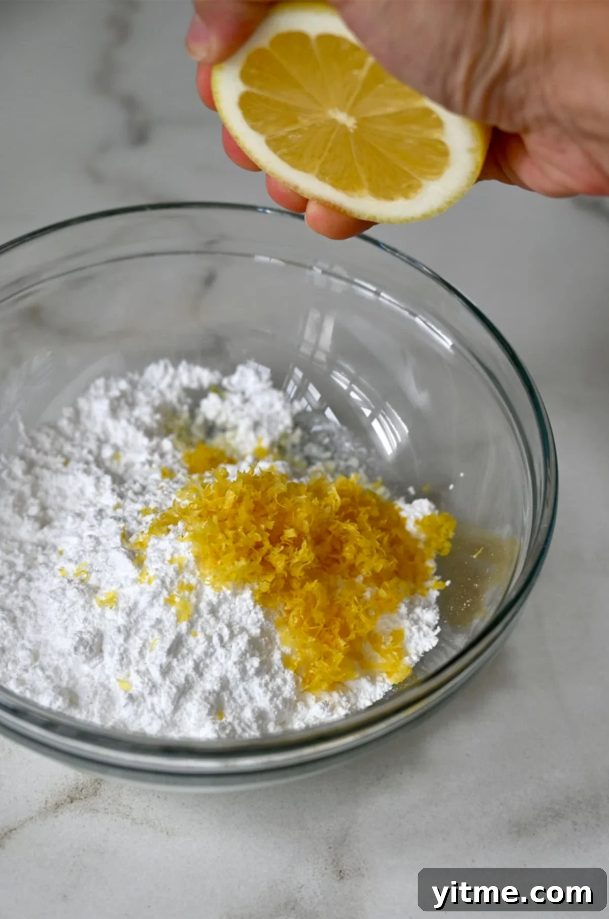 Fresh lemon juice being squeezed into a small bowl containing powdered sugar and lemon zest, preparing the glaze.