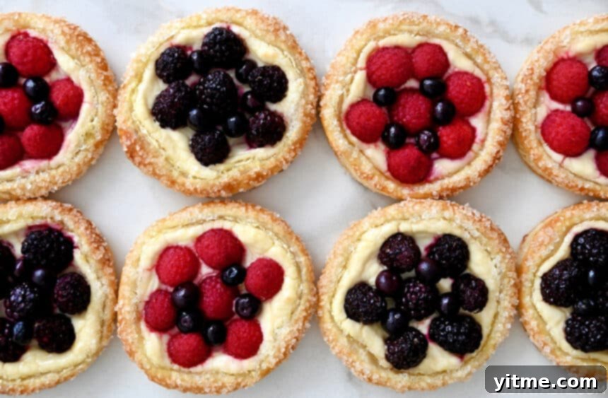 A vibrant top-down view of easy cream cheese pastries, generously topped with an assortment of fresh raspberries, blueberries, and blackberries, showcasing their colorful and inviting appeal.