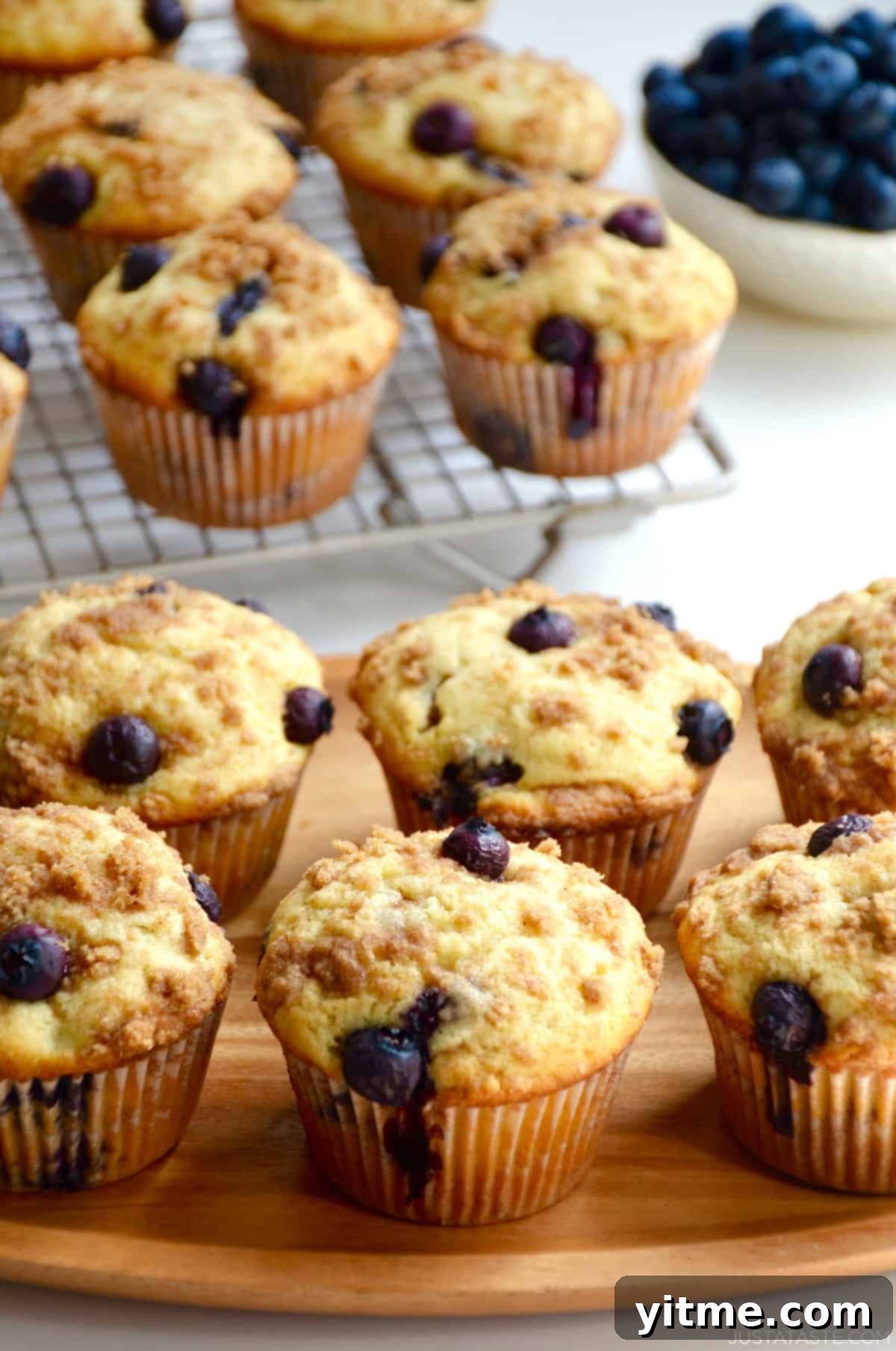 Crumb-Topped Blueberry Muffins 2 Blueberry muffins with crumb topping on a wood serving platter.