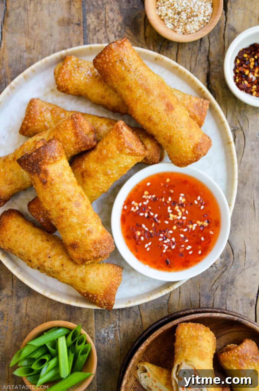 Homemade Sesame Chicken Egg Rolls served with sweet chili sauce and garnishes.