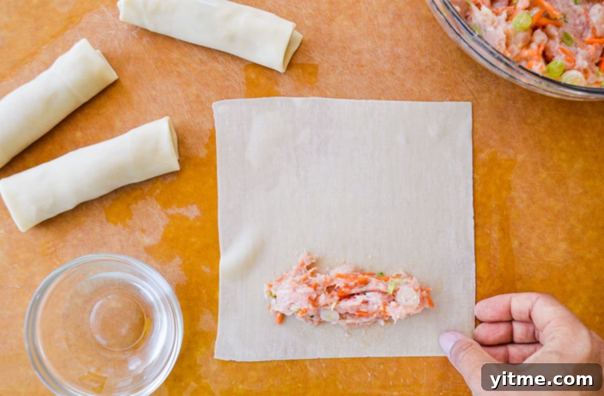 Filling egg rolls: A ground chicken mixture on an egg roll wrapper with rolled egg rolls in the background.