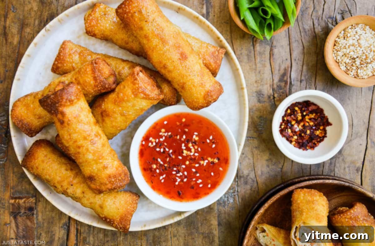 Close-up of crispy sesame chicken egg rolls with sweet chili sauce.