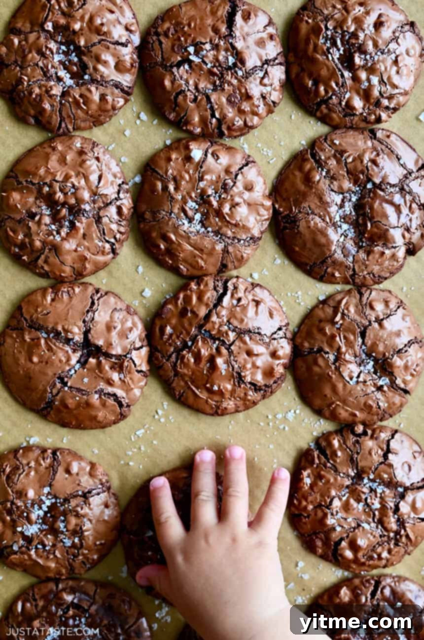 A child's hand reaches for a flourless cookie with chocolate chips topped with large-flake sea salt