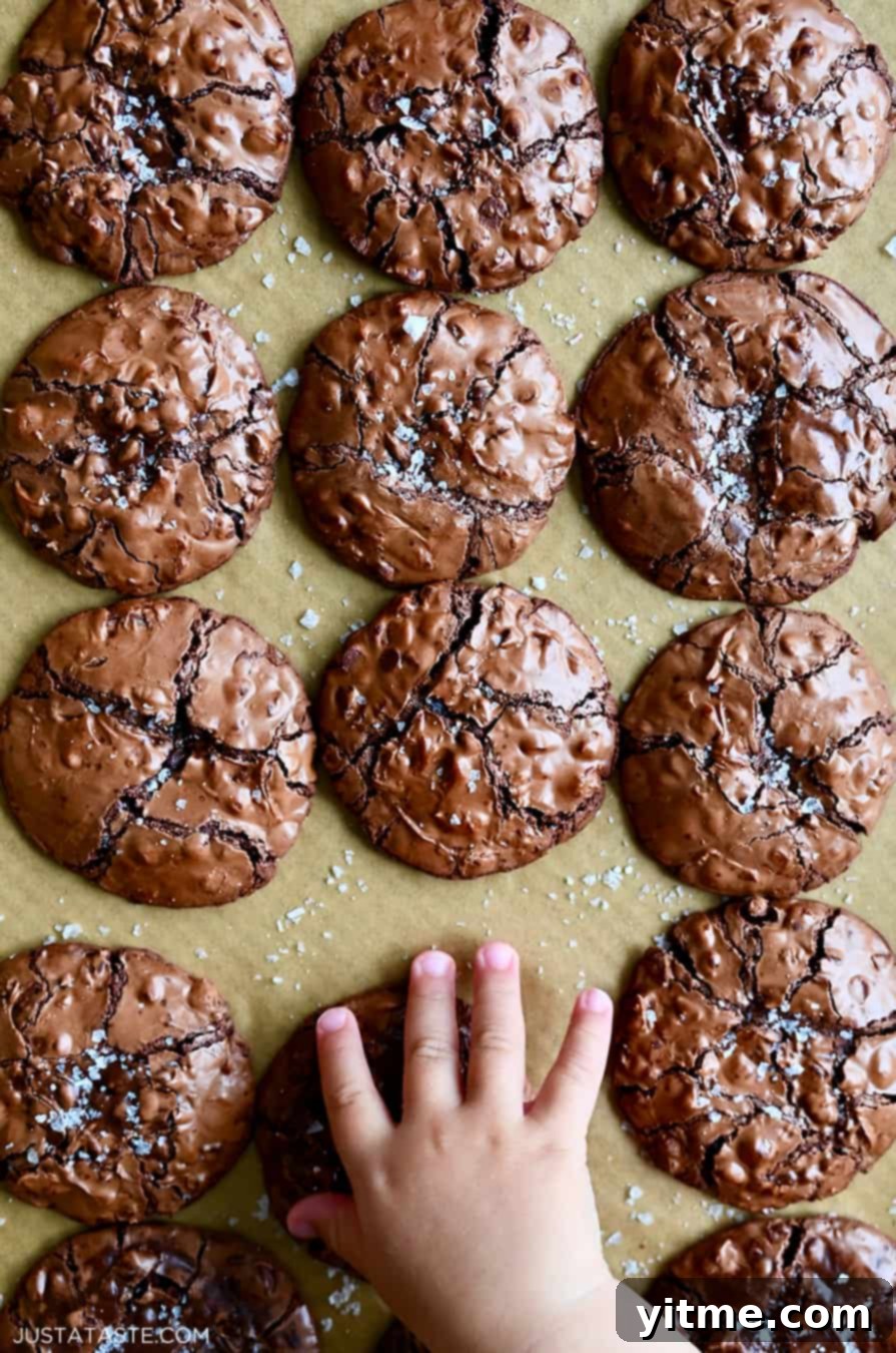 A child's hand reaches for a flourless cookie with chocolate chips topped with large-flake sea salt
