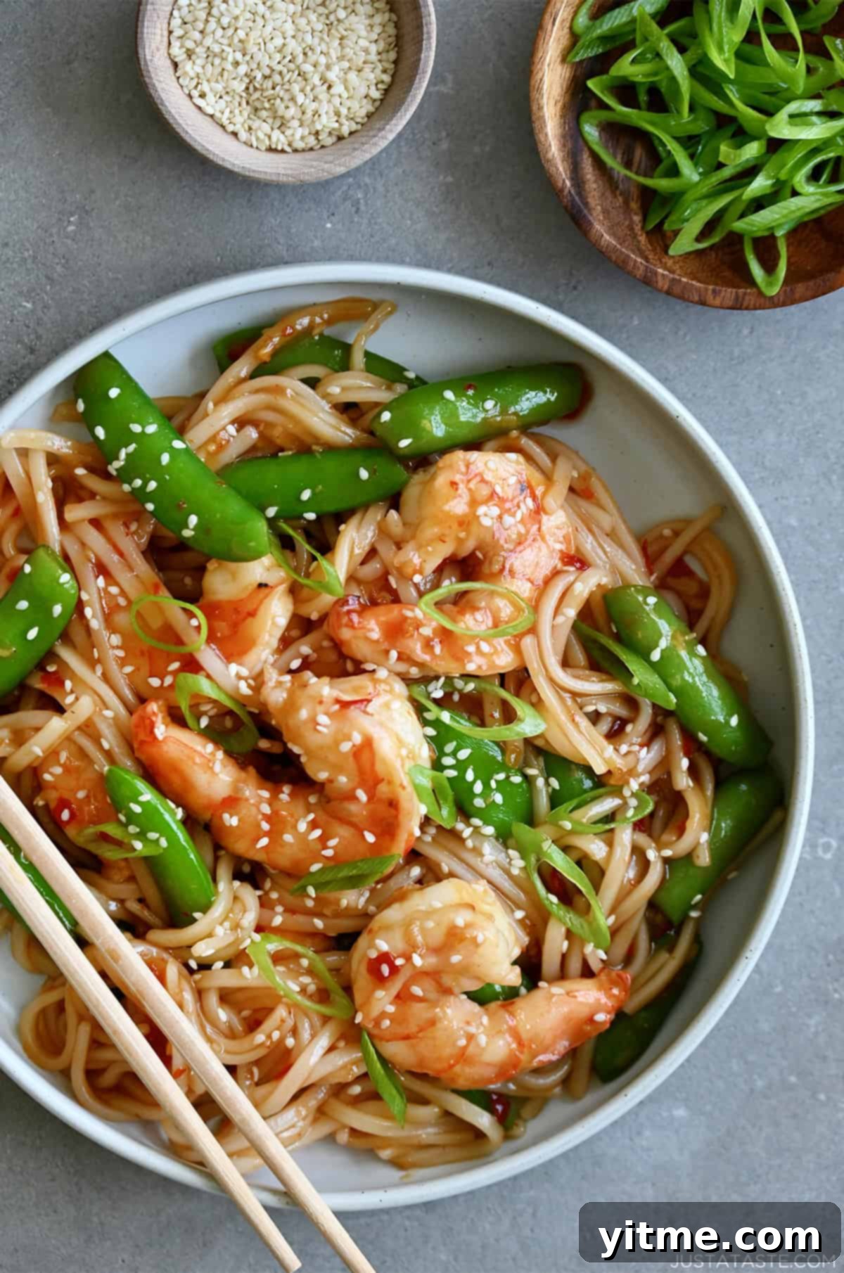 Stir-fried sweet and sour shrimp with snap peas and sesame seeds over rice noodles.