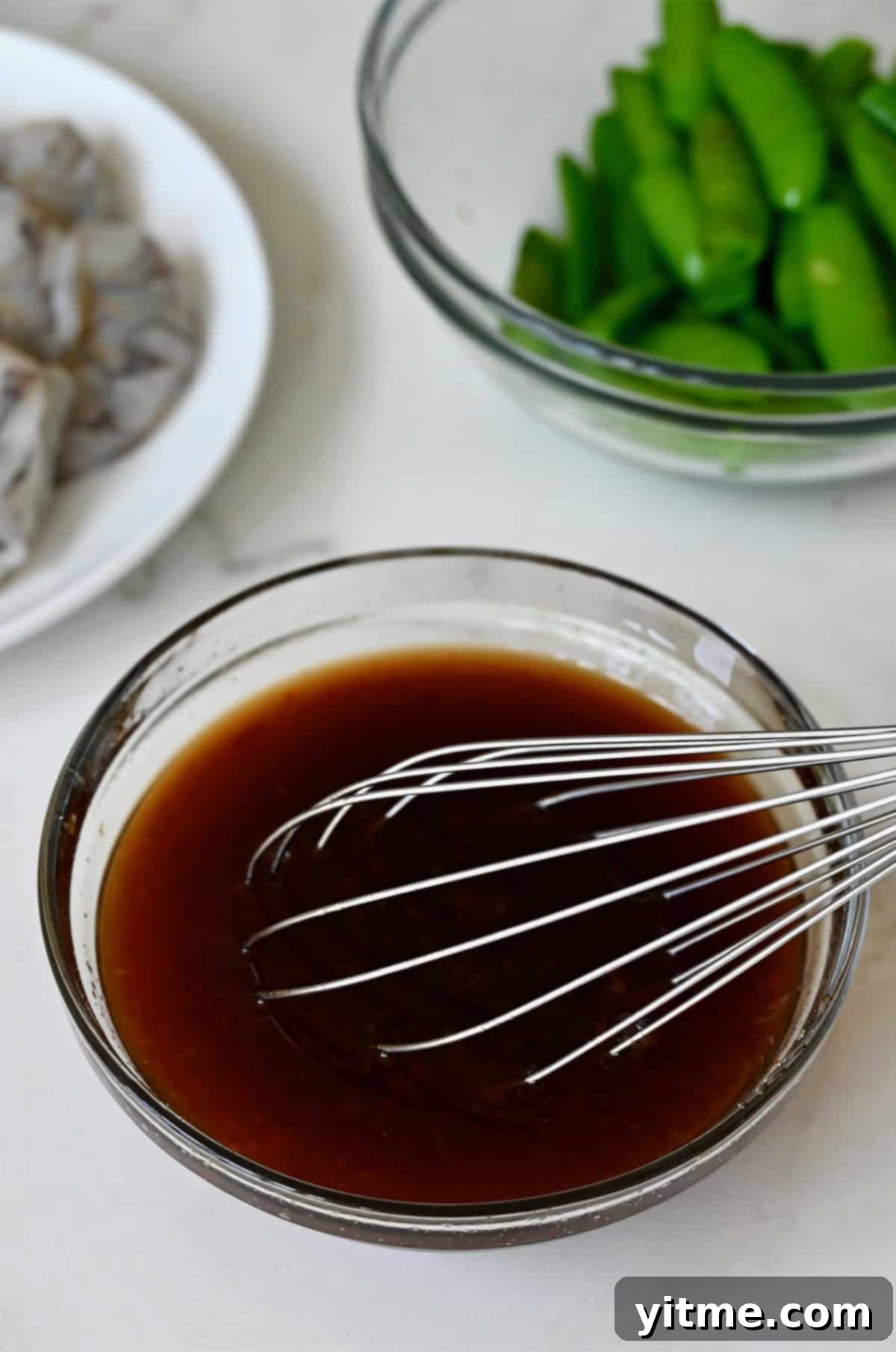 Sweet and sour sauce in a glass bowl with a whisk.