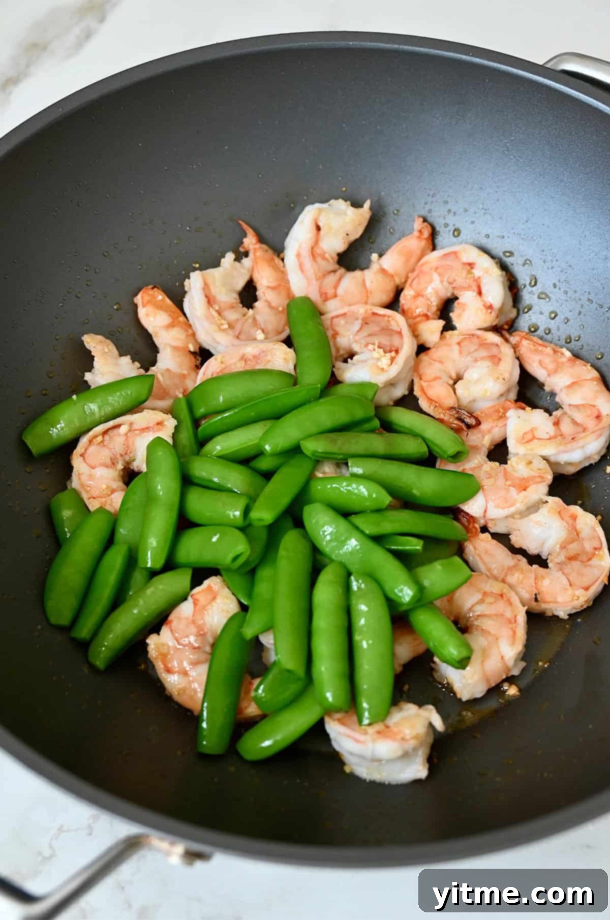 Sautéed shrimp, minced garlic and snap peas in a wok.