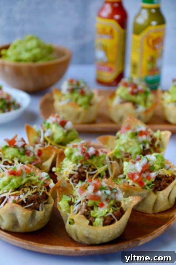 Easy Taco Salad Cups presented on a wooden serving plate, accompanied by hot sauce and creamy guacamole in the background, creating a visually appealing and delicious appetizer arrangement.