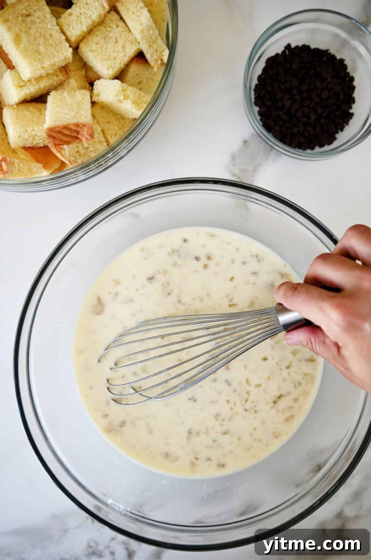 Mashed banana egg custard in a glass bowl being whisked until smooth.