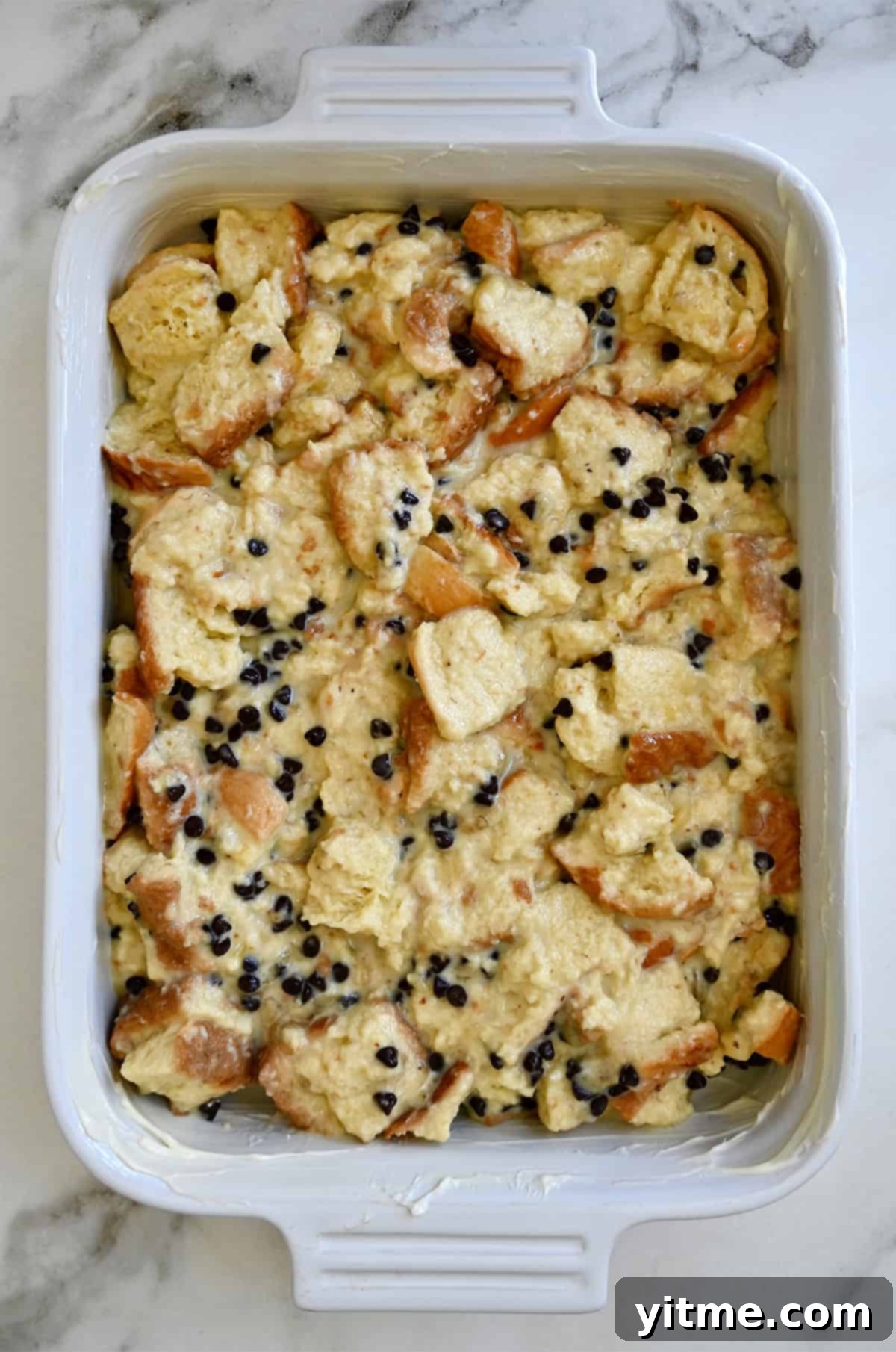 Unbaked bread pudding mixture evenly spread in a baking dish, with mini chocolate chips visible.