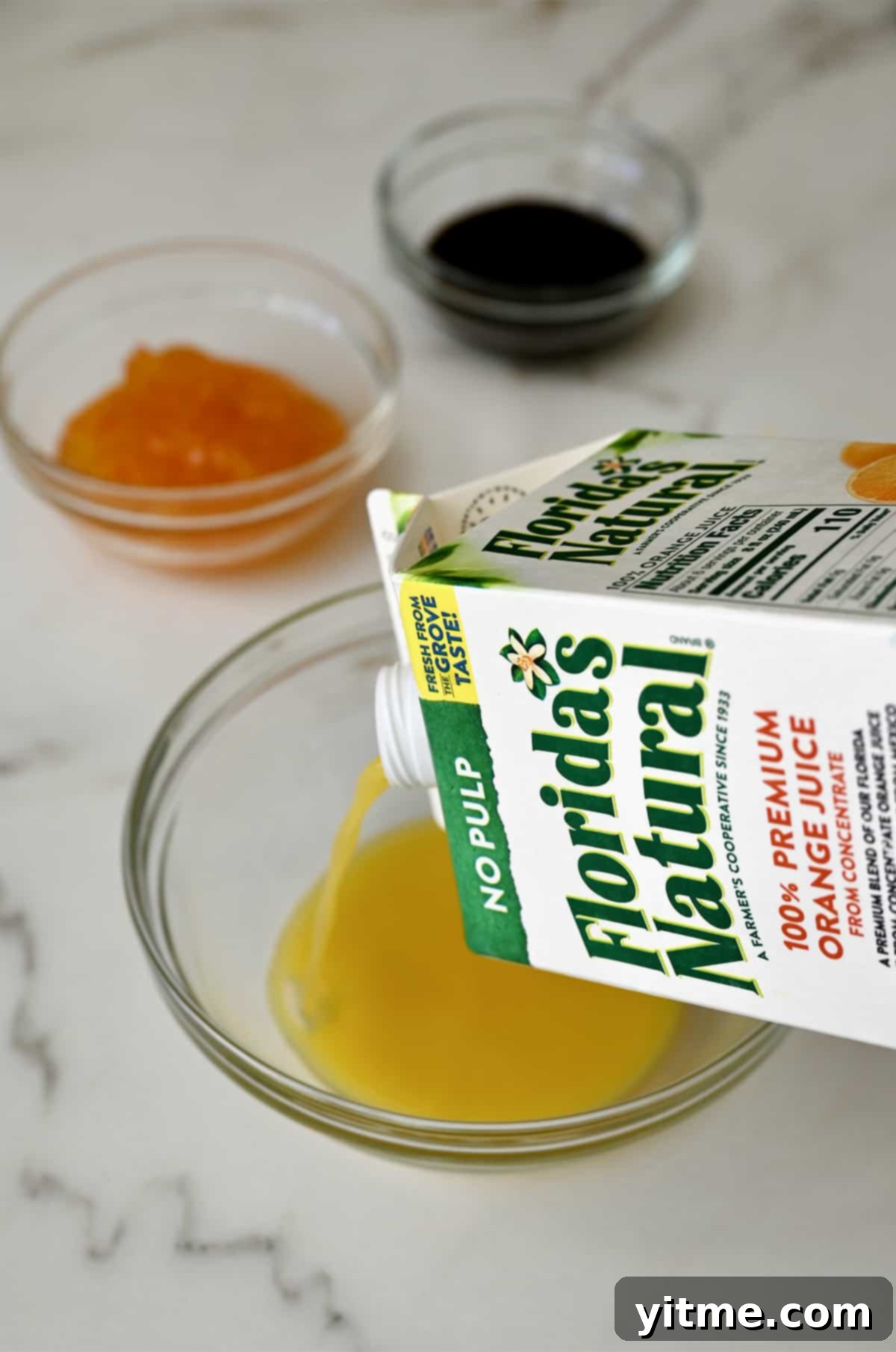 Citrus Glazed Baked Chicken Strips 4 Orange juice being poured from a carton into a clear bowl, highlighting its fresh, vibrant color.