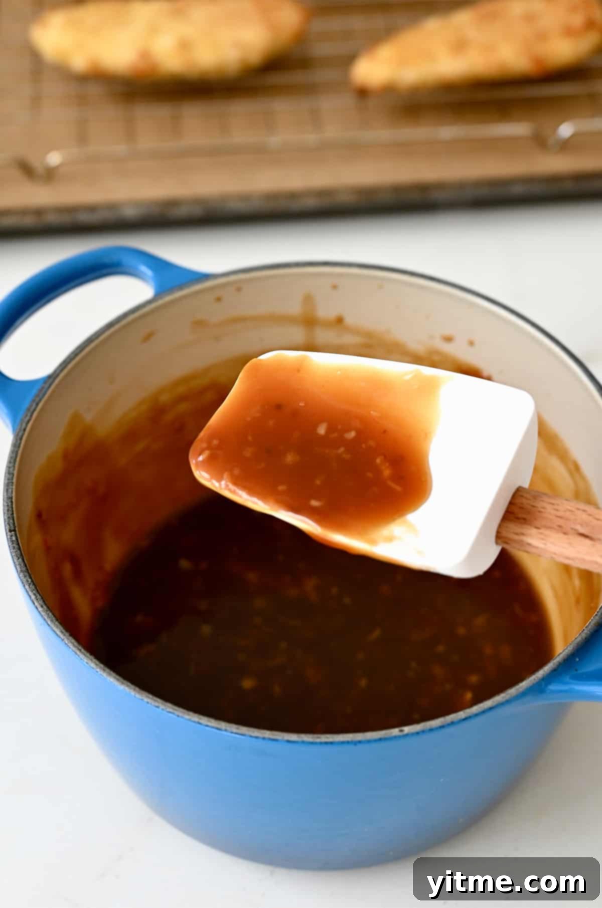 Citrus Glazed Baked Chicken Strips 5 A spatula stirring thick orange chicken sauce in a saucepan on the stove.