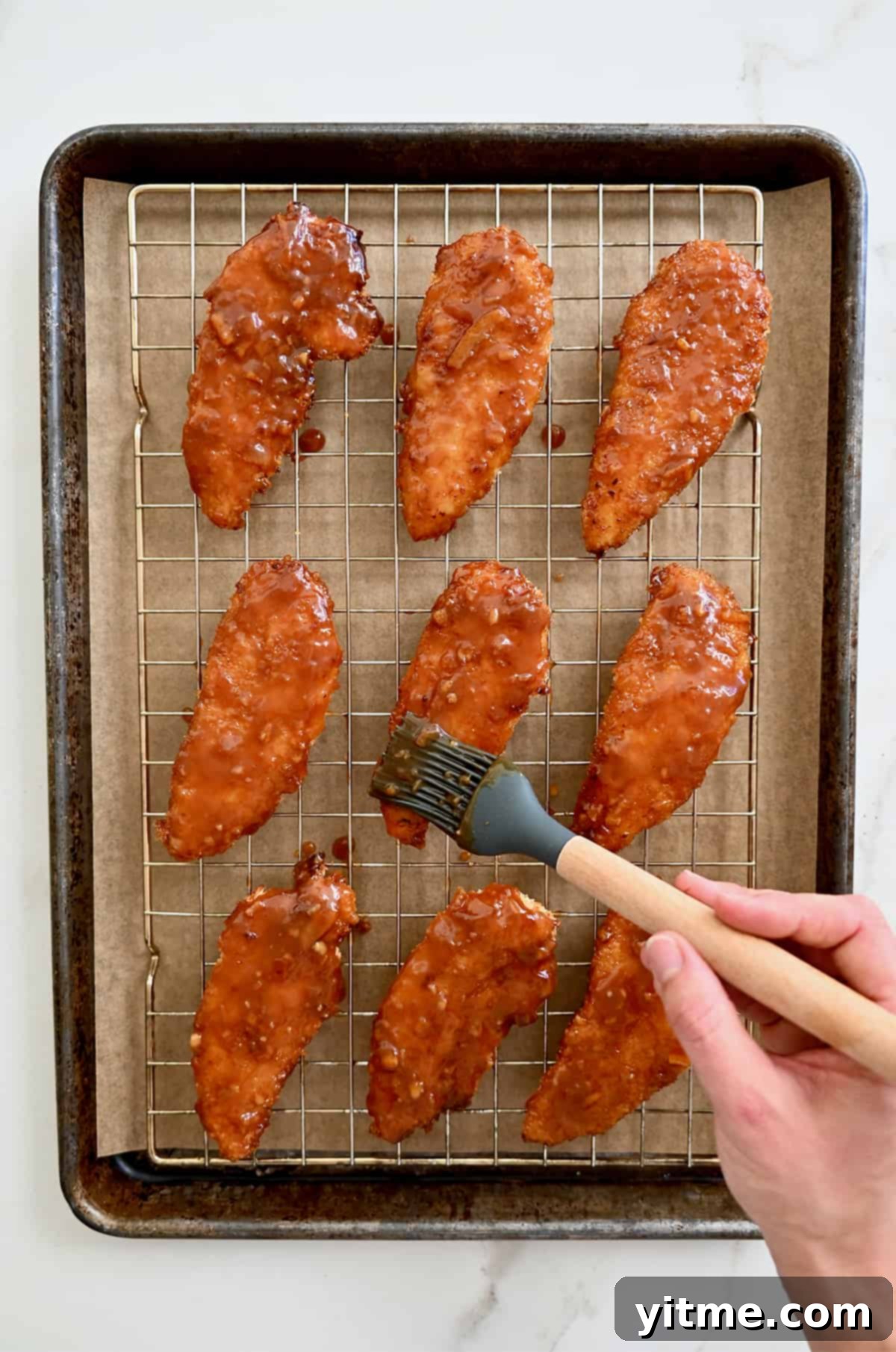 Citrus Glazed Baked Chicken Strips 6 Orange sauce being brushed atop baked chicken tenders on a wire rack on a baking sheet, showcasing the sticky glaze.