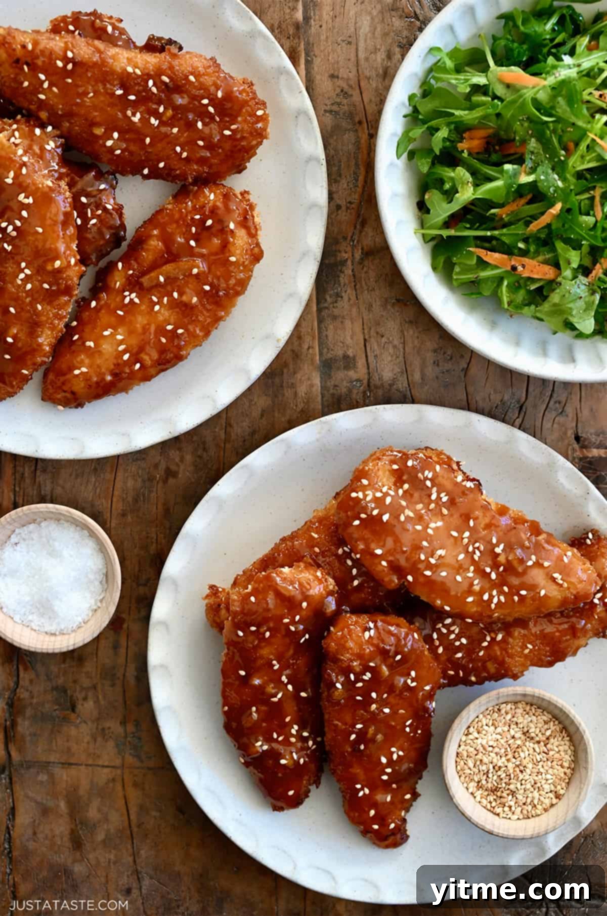 Citrus Glazed Baked Chicken Strips 7 Orange chicken tenders on a plate garnished with sesame seeds next to a plate topped with mixed salad greens, illustrating a complete meal.