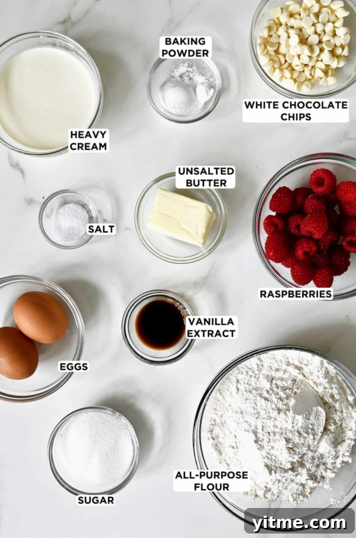 Raspberry Bliss Scones 3 Ingredients for making raspberry scones, including flour, butter, cream, raspberries, and white chocolate chips, arranged in glass bowls.