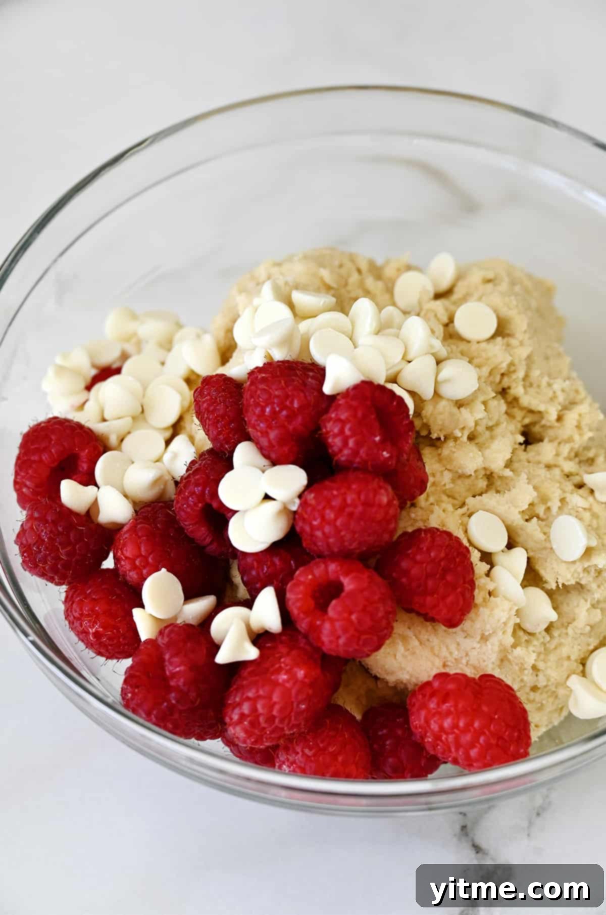 Raspberry Bliss Scones 4 A glass bowl filled with scone dough, fresh raspberries, and white chocolate chips ready to be mixed.