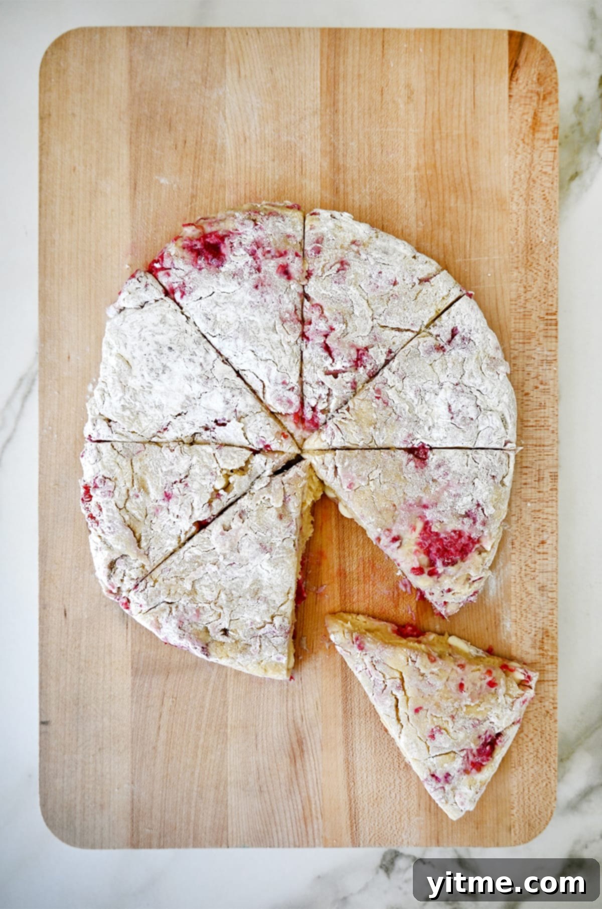 Raspberry Bliss Scones 5 A disc of raspberry scone dough cut into 8 wedges on a wooden cutting board, ready for baking.