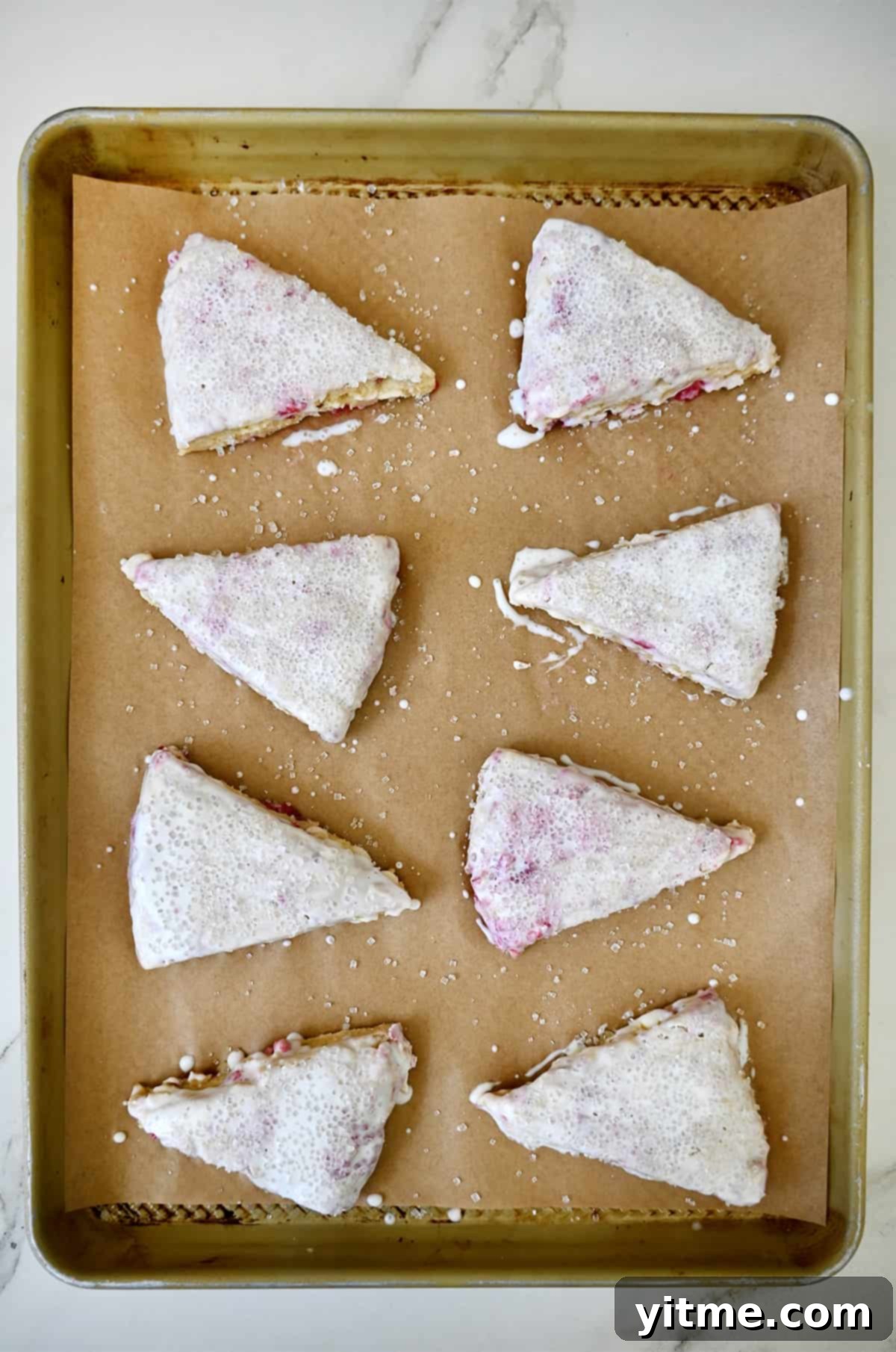 Raspberry Bliss Scones 6 Unbaked raspberry scones brushed with heavy cream on a baking sheet lined with parchment paper.