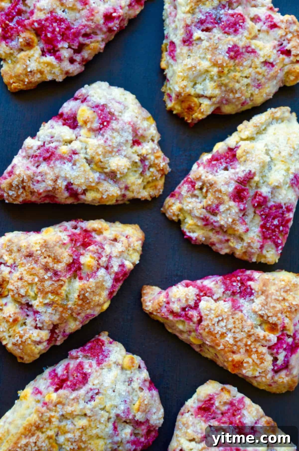 Raspberry Bliss Scones 7 Delicious baked raspberry white chocolate chip scones sprinkled with sanding sugar on a dark background.