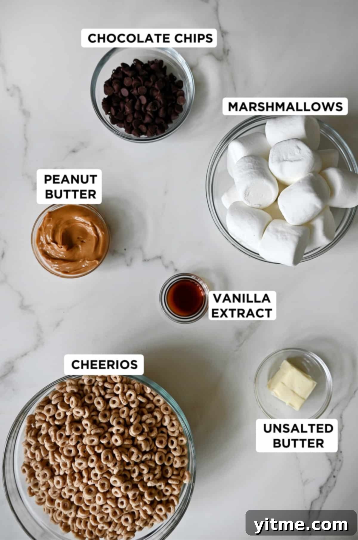 Peanut Butter Cheerios Marshmallow Bars 3 A collection of bowls displaying the six simple ingredients for peanut butter Cheerios treats: chocolate chips, marshmallows, unsalted butter, vanilla extract, Cheerios, and creamy peanut butter.